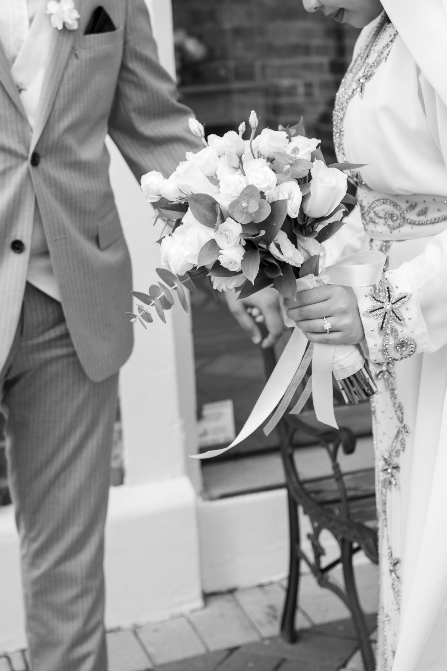 Black and white wedding photo showing bridesmaids holding white bouquets while standing in a row along a white fence.
