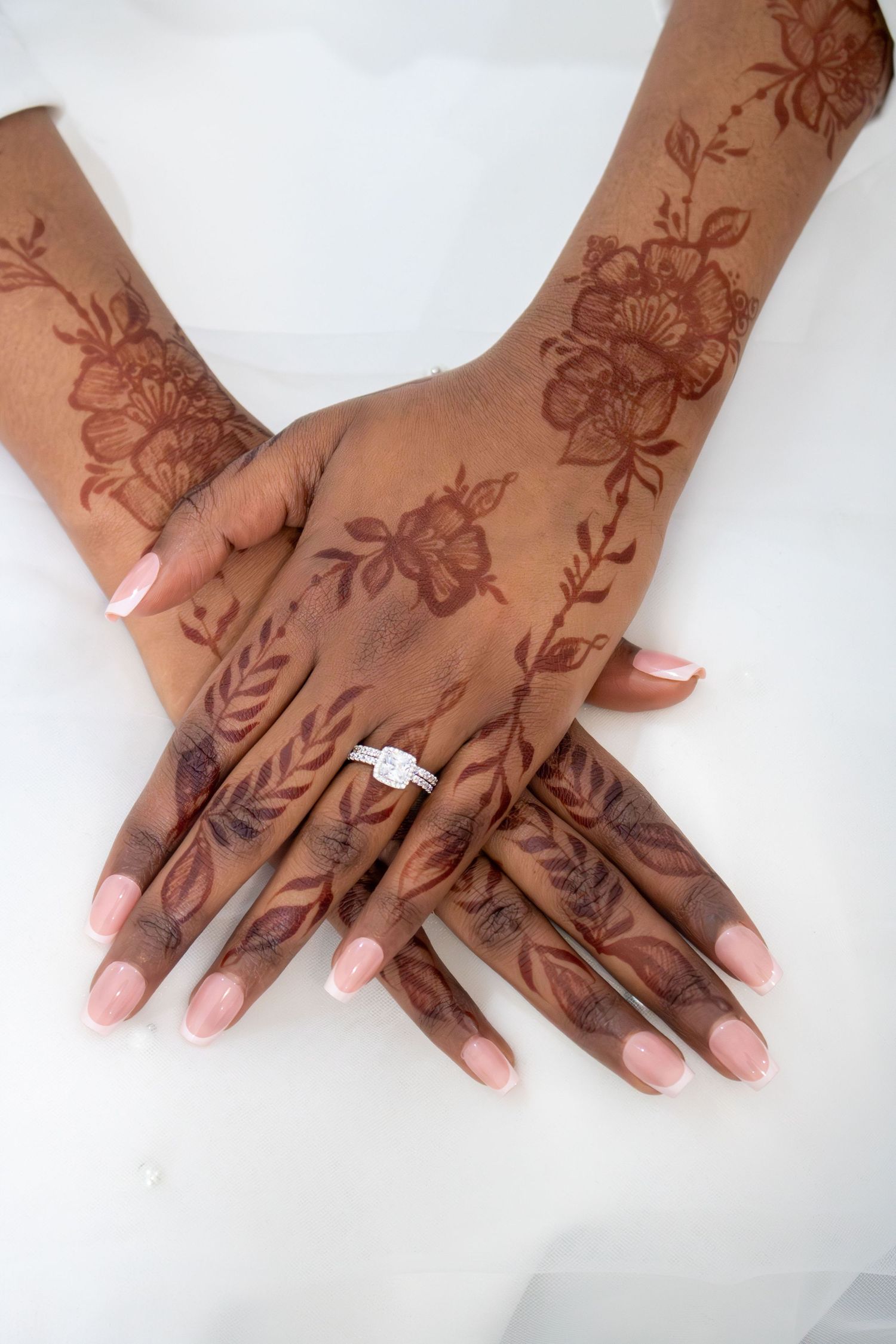 Hands adorned with intricate floral henna designs and an engagement ring displayed against a white background.