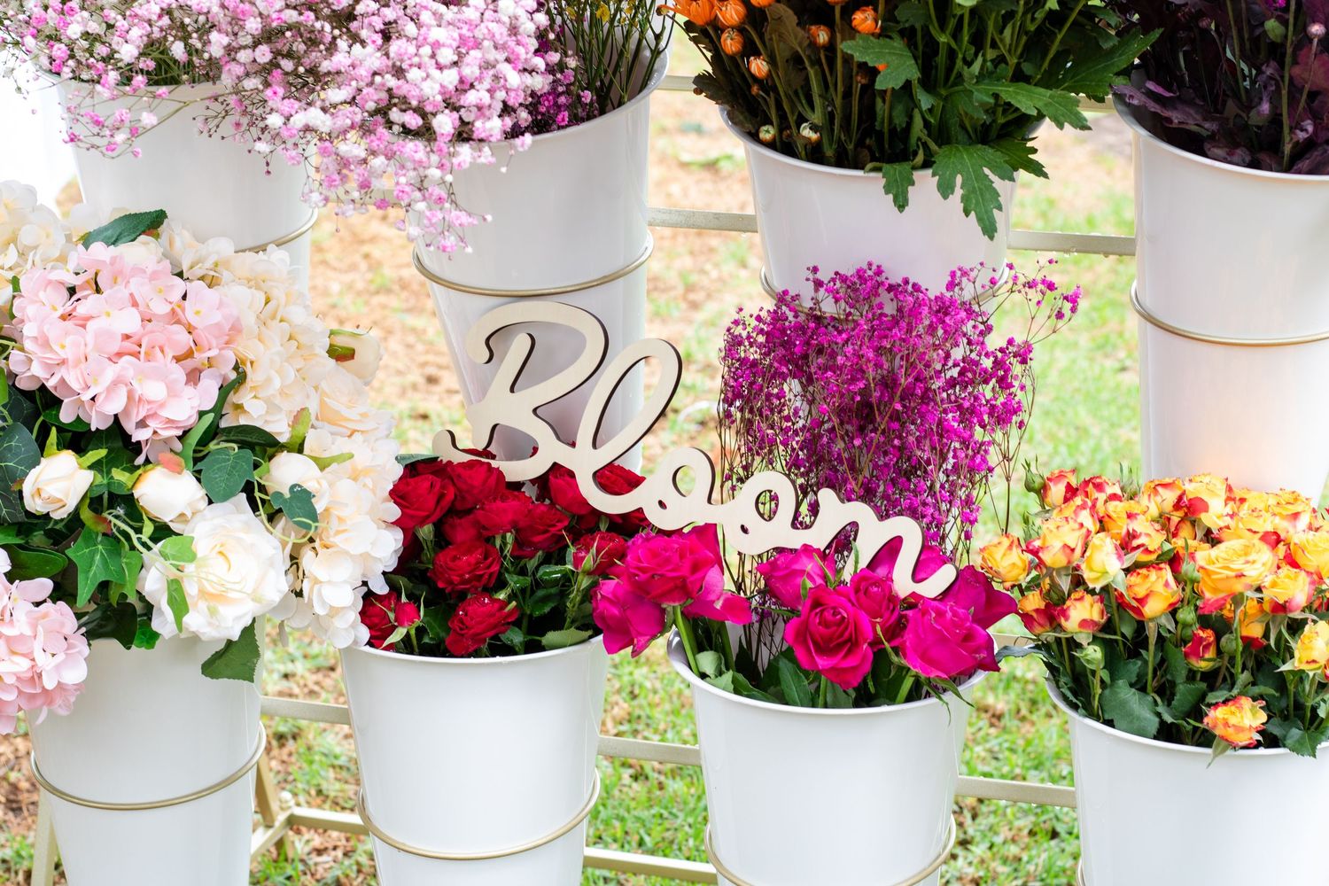 A collection of colorful potted flowers including pink, red, and orange blooms arranged in white containers outdoors.
