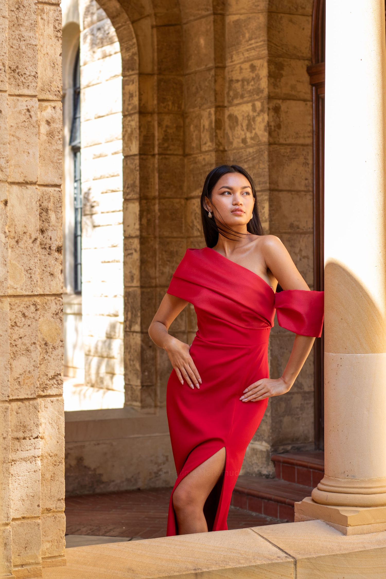 A dancer in a flowing red dress performs elegant poses among stone columns in a historic building.