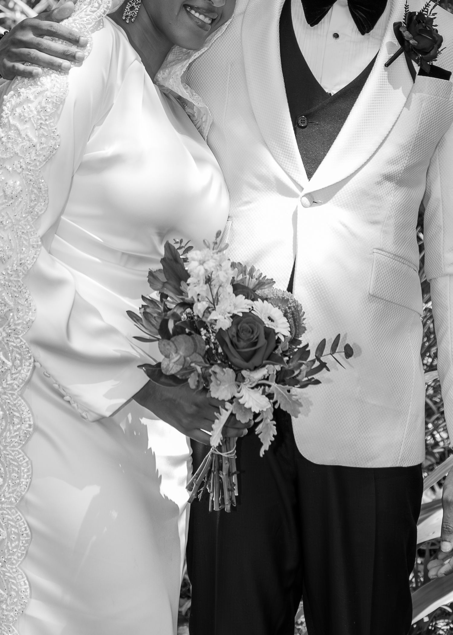 Black and white photo of a bride and groom posing together, bride holding a bouquet of roses and flowers.