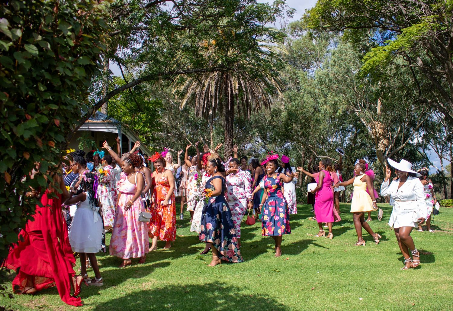A large group of people in colorful traditional dresses gather outdoors for a cultural celebration in a park setting.