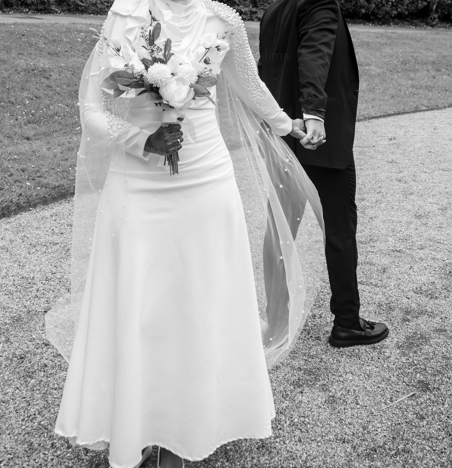Black and white wedding photo showing bride in flowing white dress and veil holding bouquet next to groom in dark suit.