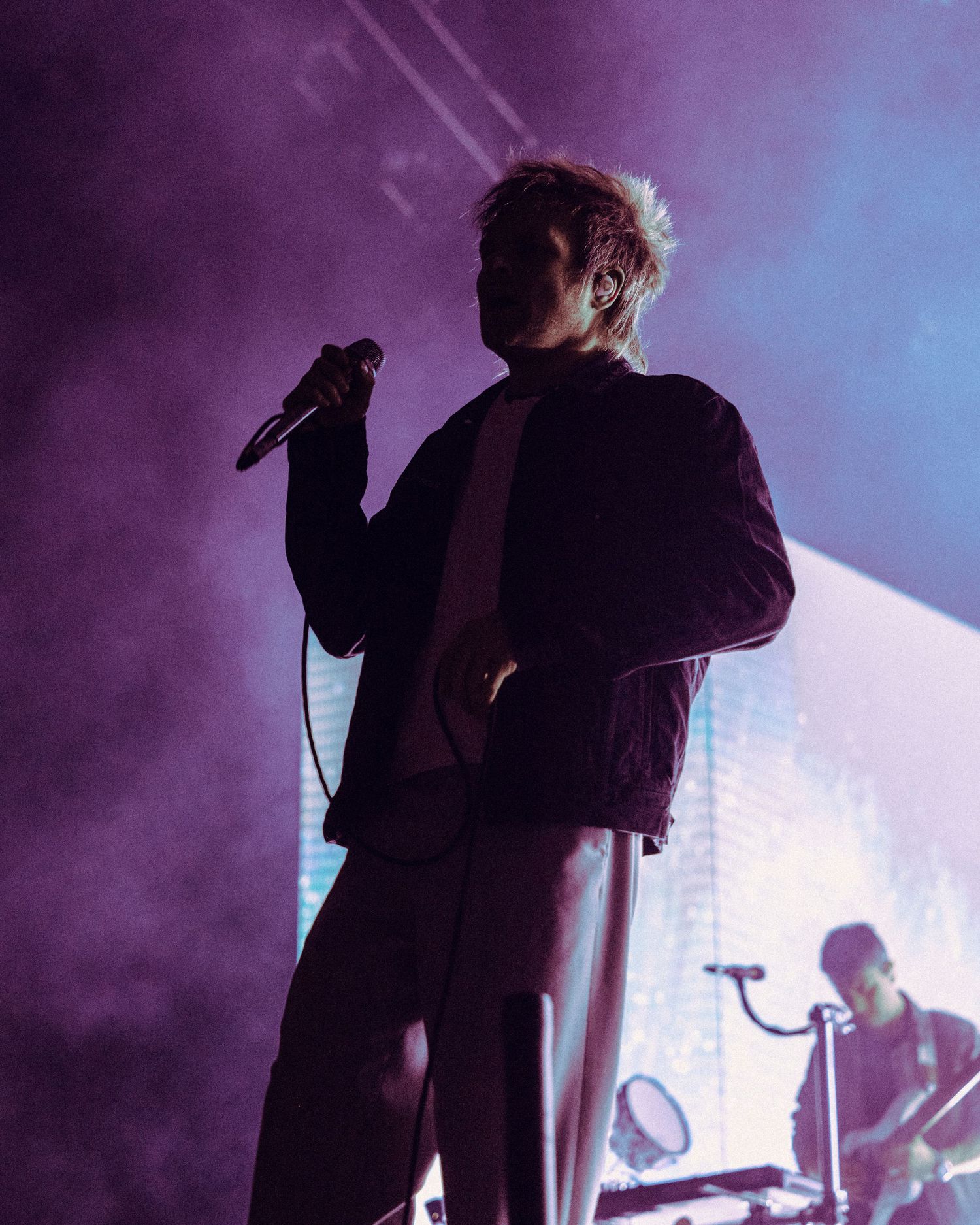 Silhouetted figures perform on a dimly lit stage with purple and blue atmospheric lighting and fog effects.