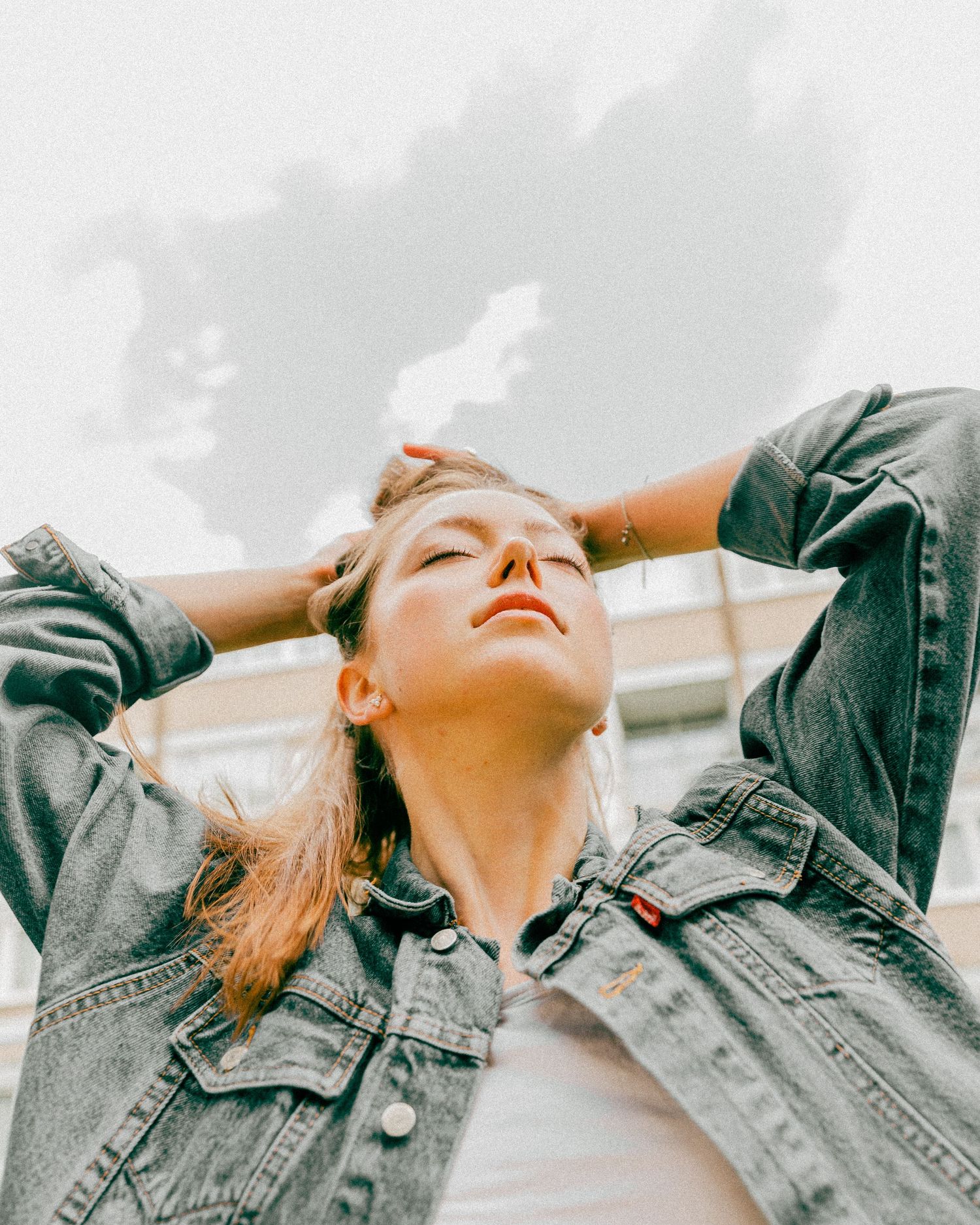 Fashion portraits against cloudy sky wearing denim jacket with dramatic upward poses.