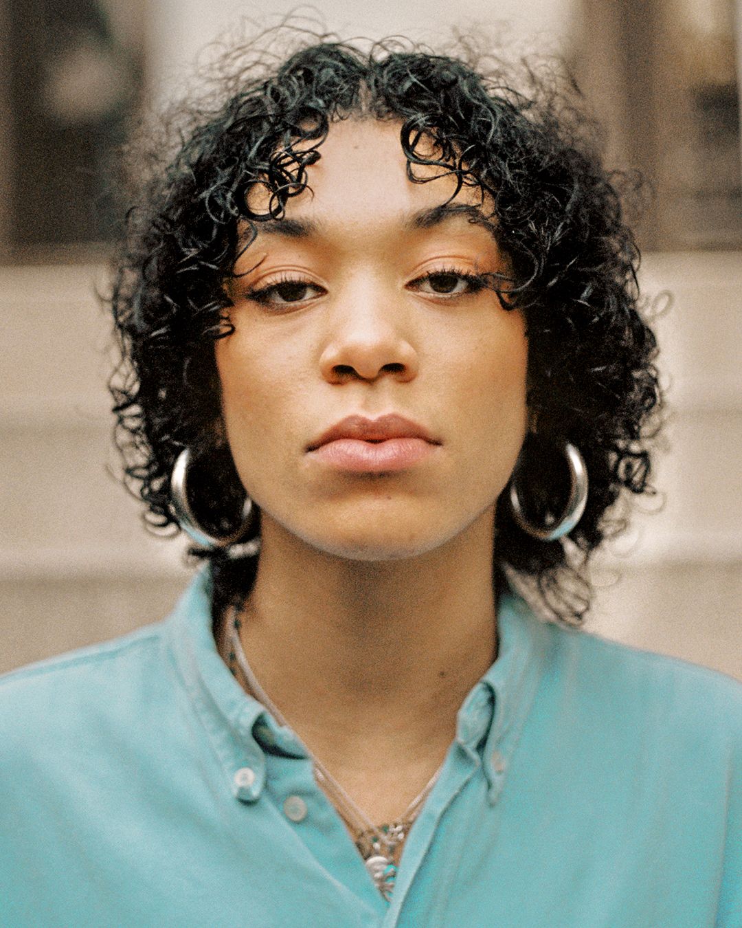 Portrait featuring curly hair, hoop earrings and light blue button-down shirt.