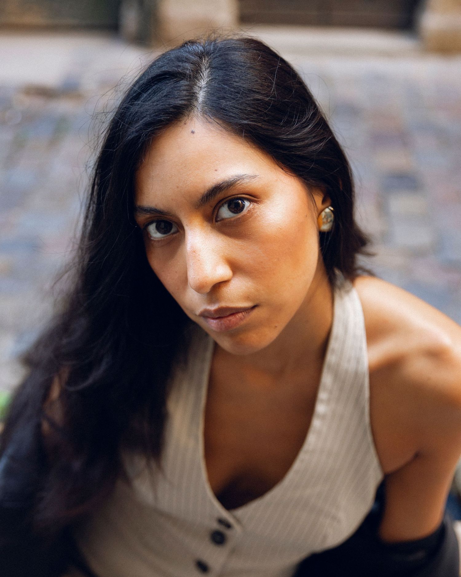 Stylish portrait series featuring white ribbed tank top and dark hair against stone wall.