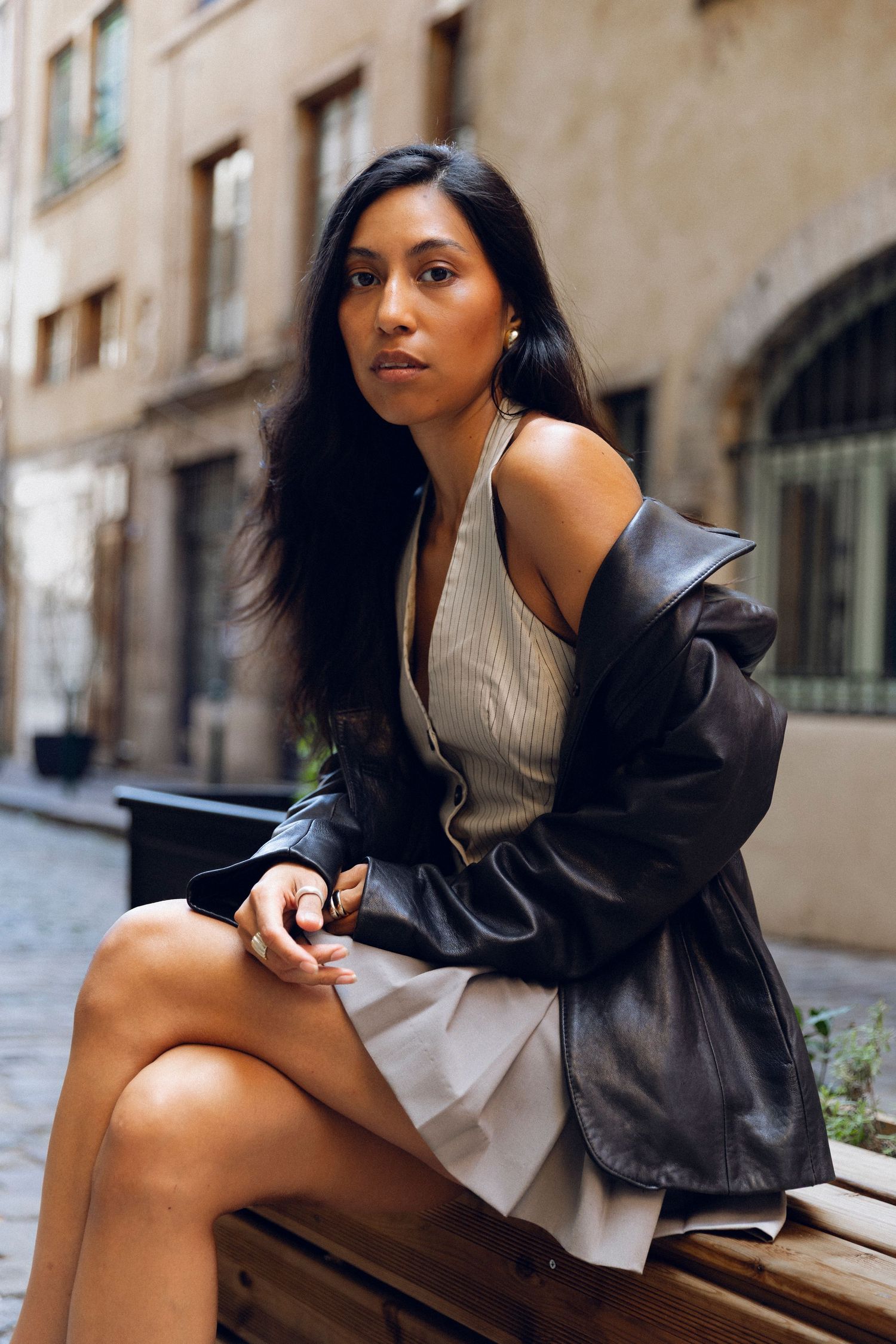 Stylish urban portrait featuring black leather coat and ribbed cream top on city street.