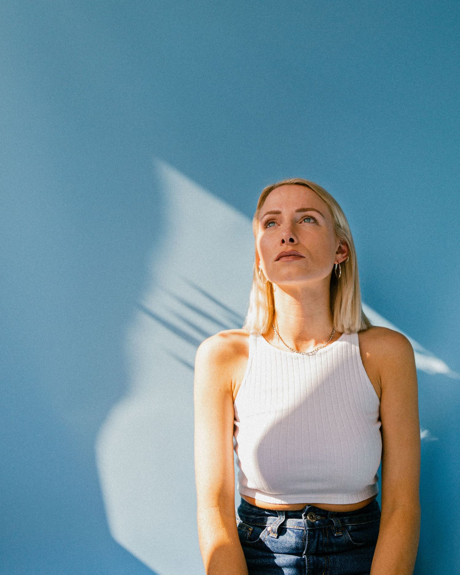 Modern portrait sequence against blue wall with striking shadow play and white tank top.