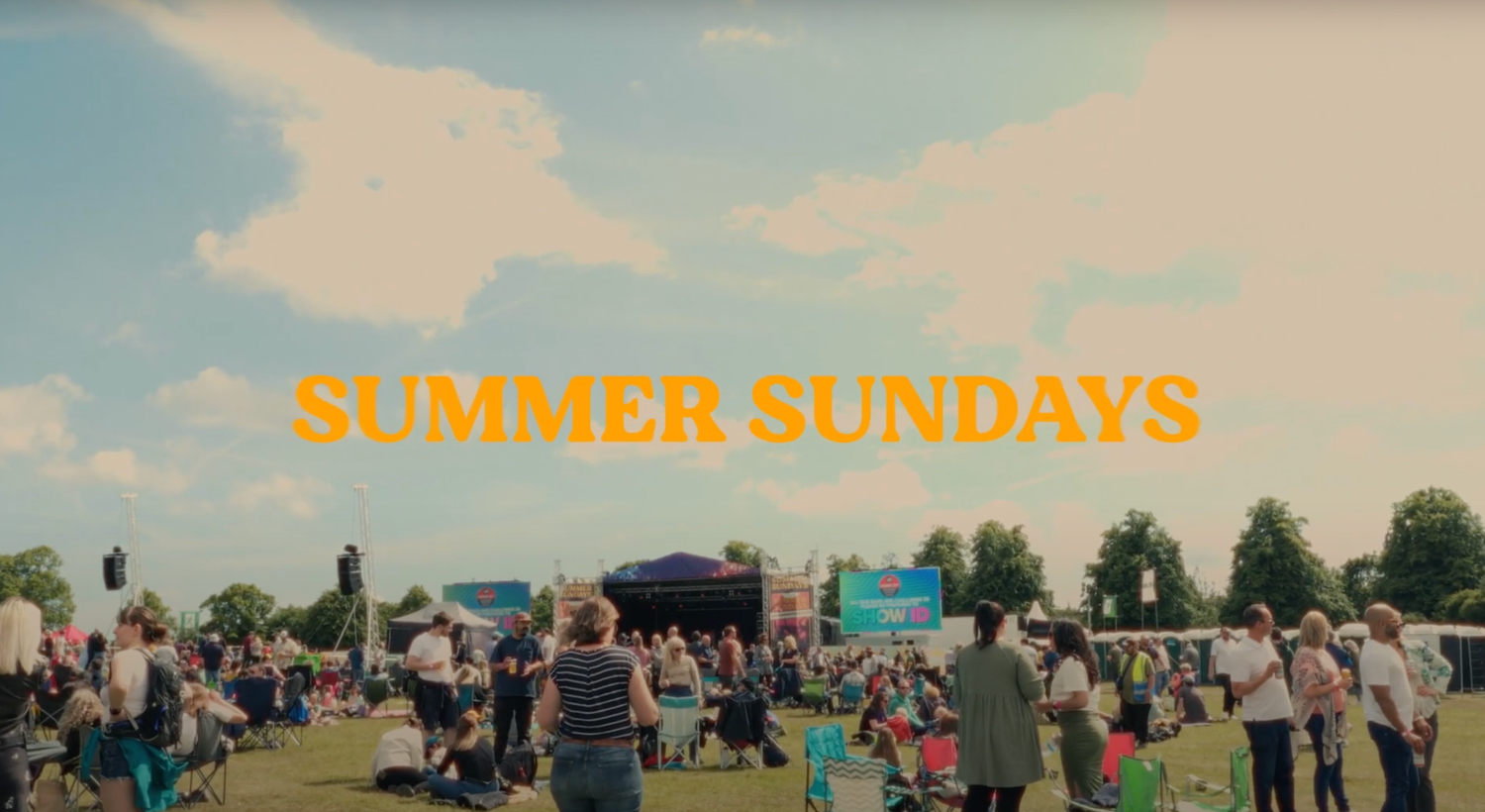 Outdoor summer festival crowd gathering under blue sky with yellow text overlay.