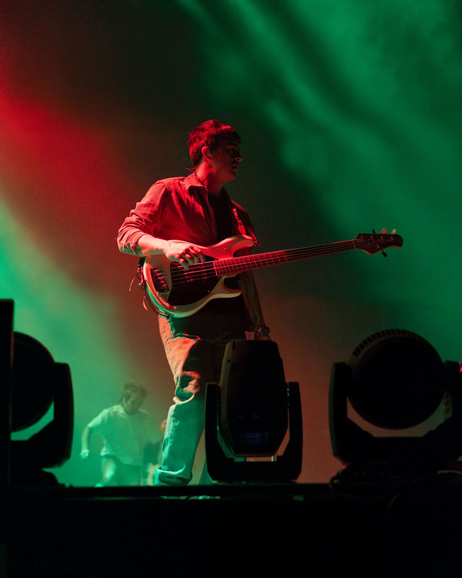 Silhouetted musician performing on stage with dramatic red and green lighting creating a moody atmospheric effect.