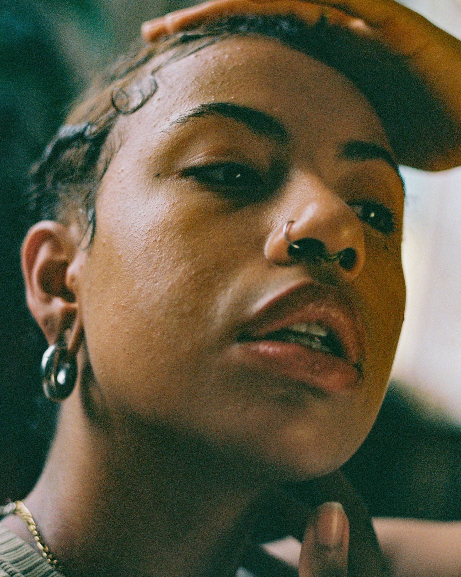 Close-up portrait showing nose ring and cap in warm natural lighting.
