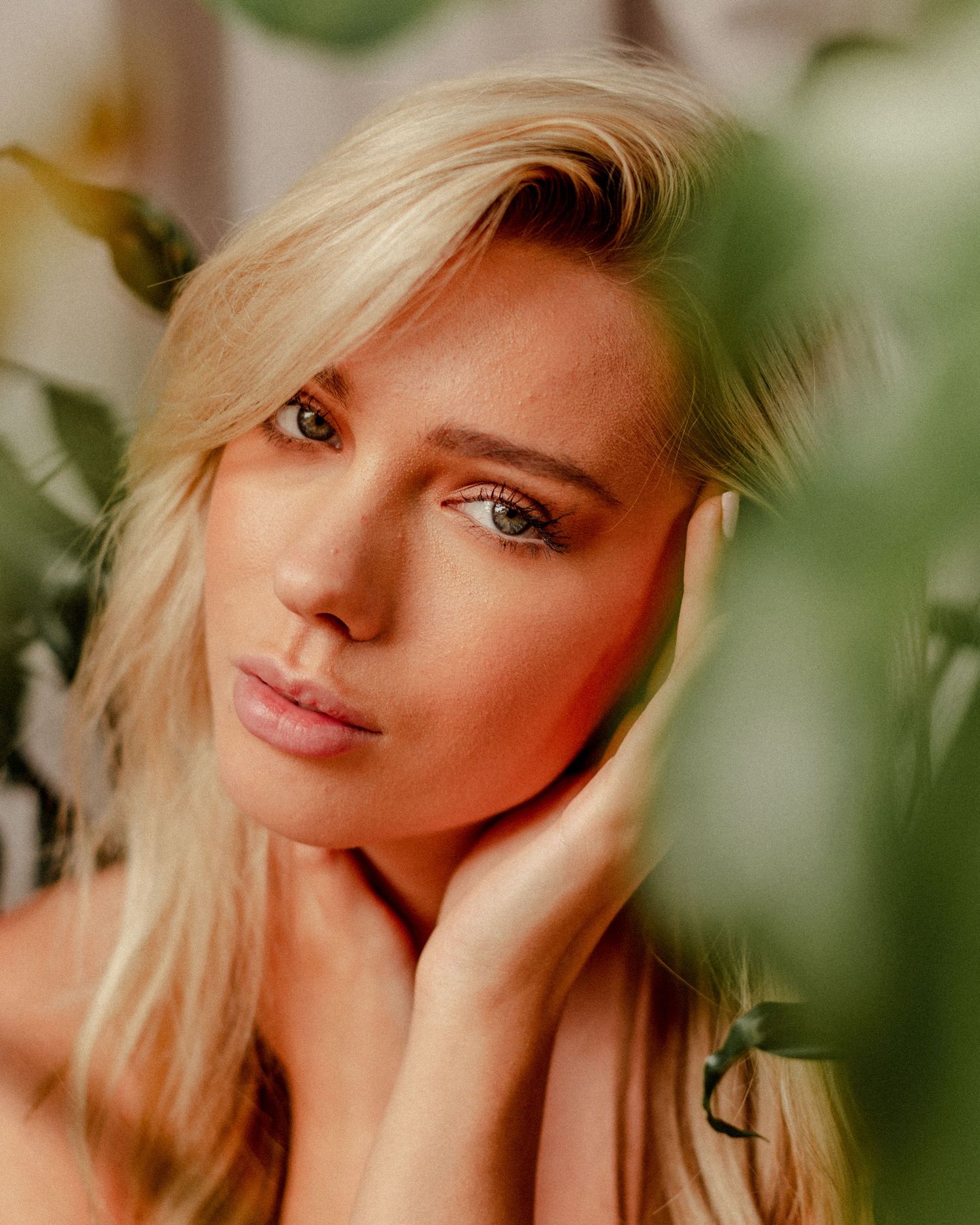 Close-up beauty portrait with dramatic lighting and natural makeup against green leaves.