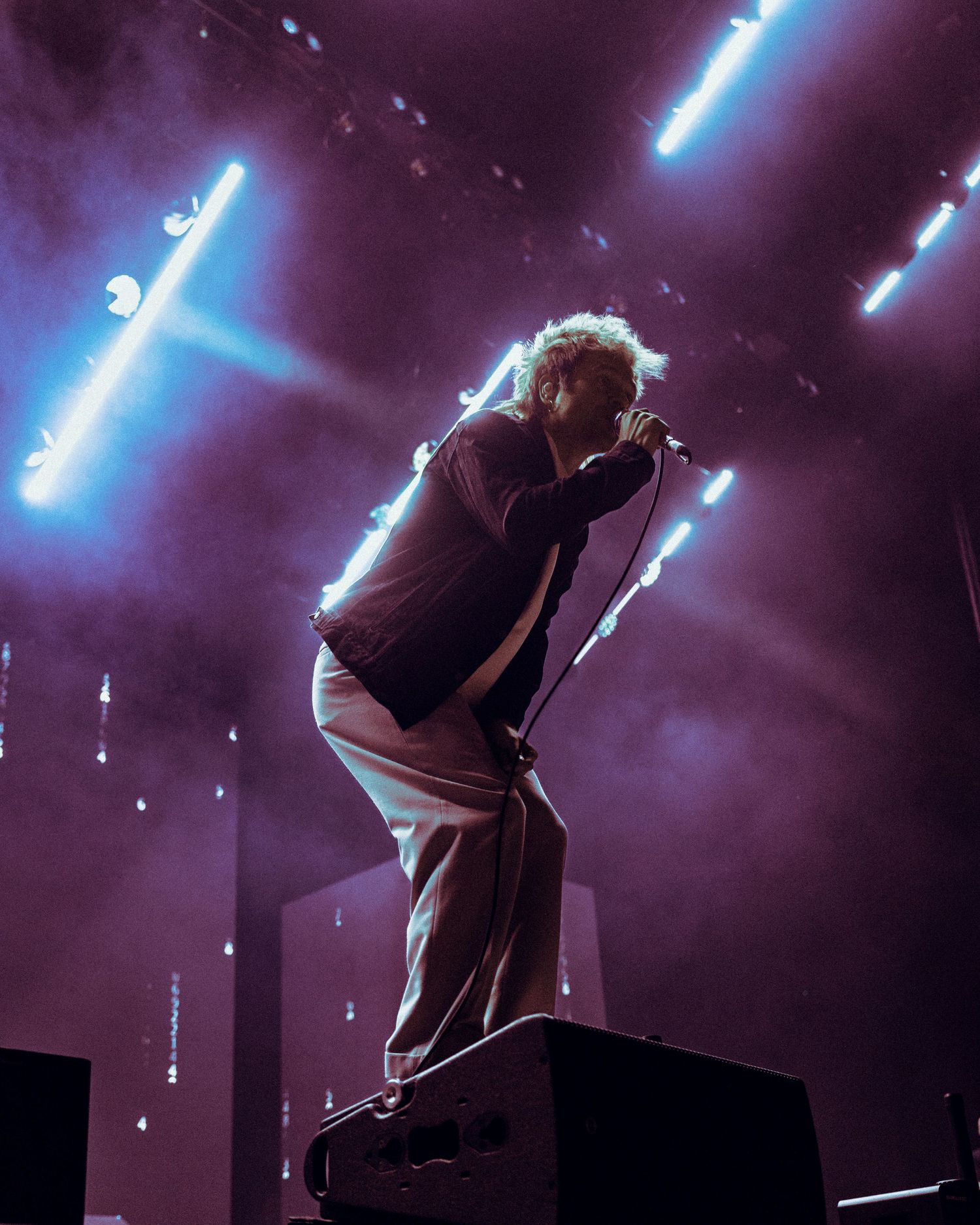 Silhouetted performer stands on stage behind microphone with dramatic blue and purple stage lighting creating moody atmosphere.