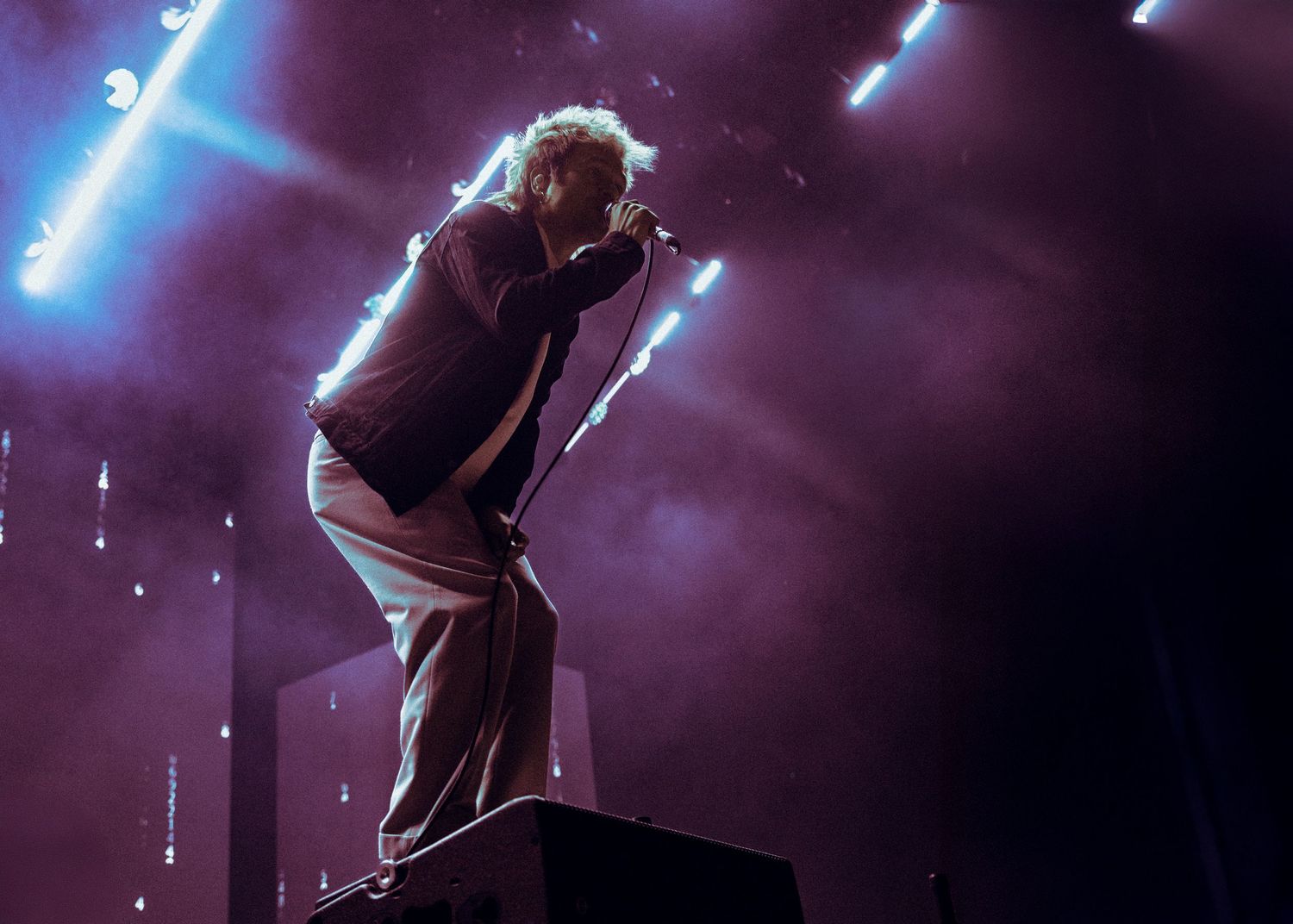 Concert performer on stage silhouetted against dramatic purple lighting and spotlights.