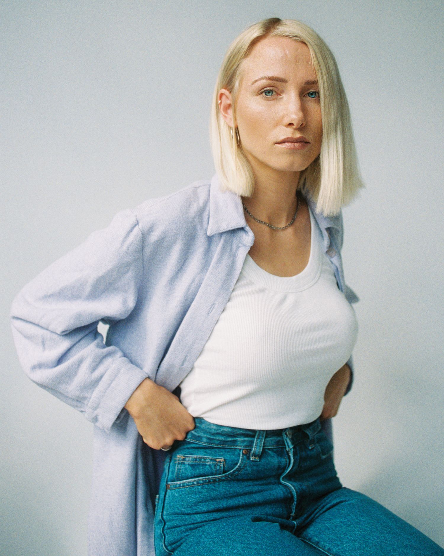 Casual fashion portrait in light blue shirt and jeans against neutral background.