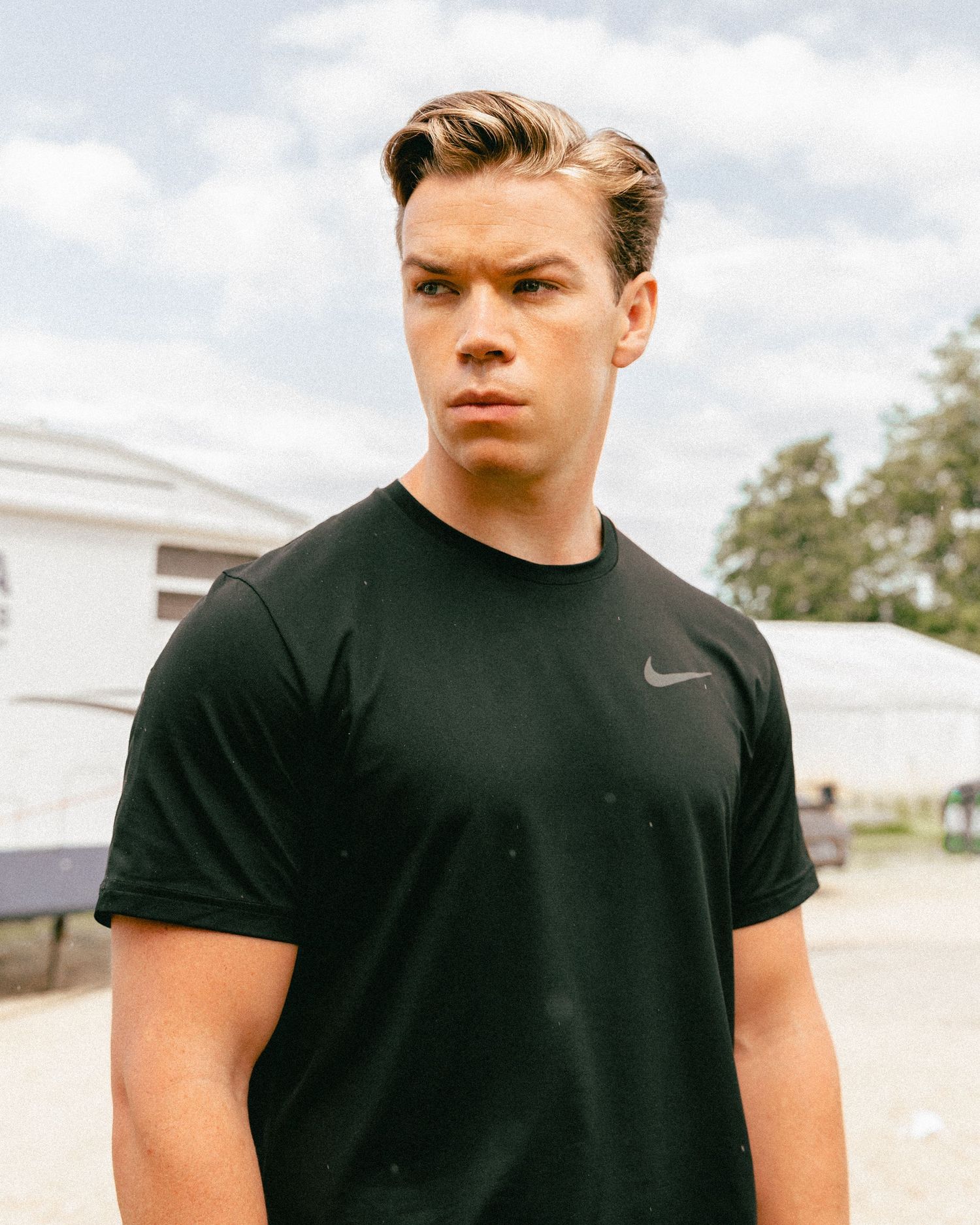 Athletic model in black Nike t-shirt poses outdoors against white building.