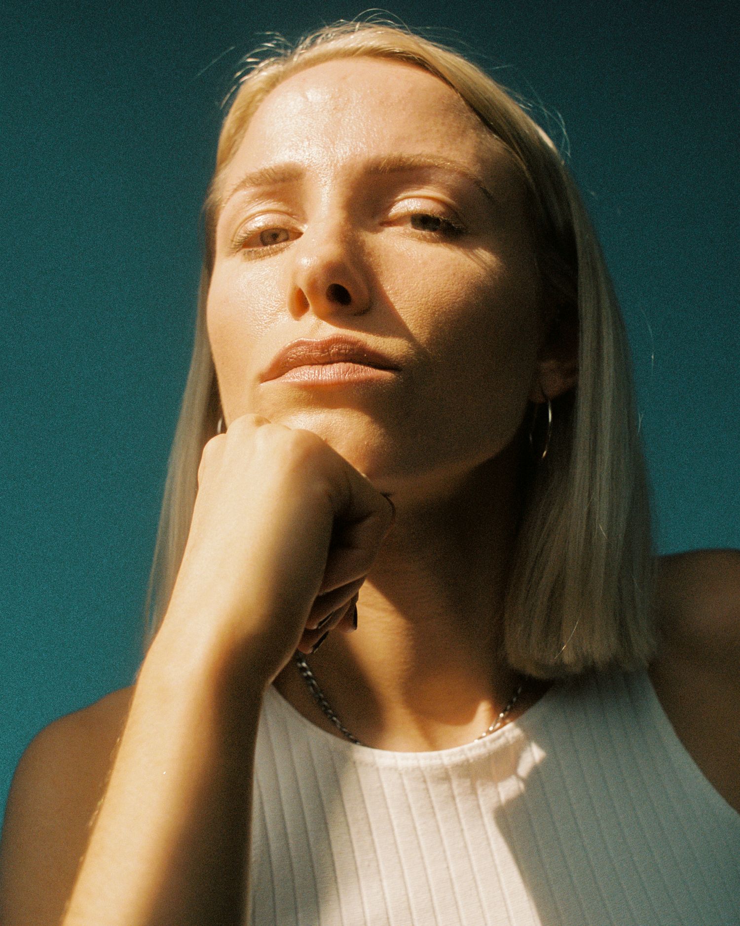 Minimalist portrait series against teal background with warm sunlight creating artistic shadows.