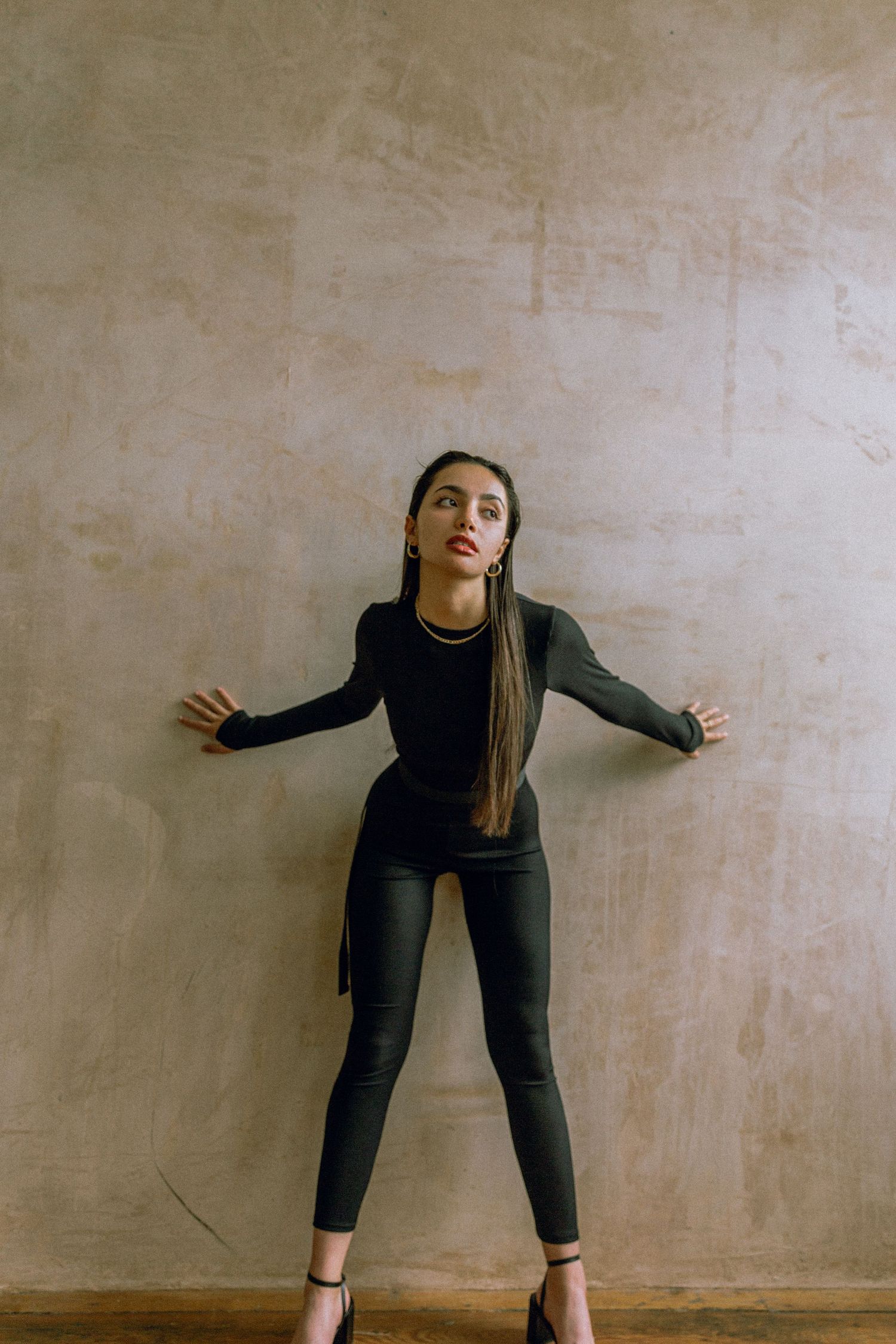 Full body fashion pose against textured beige wall wearing all black ensemble.