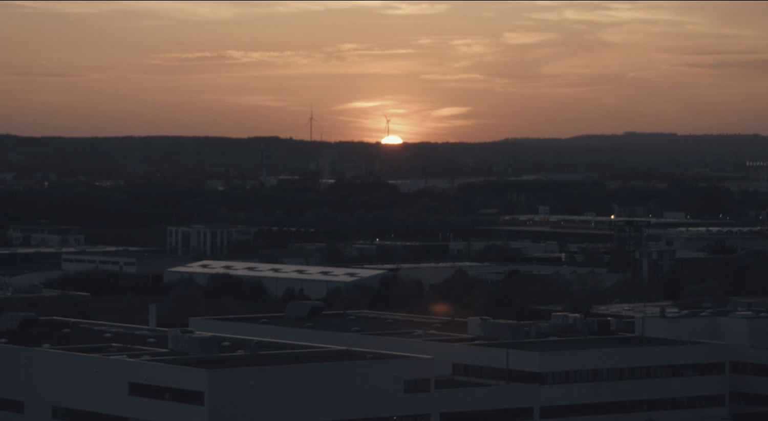 Scenic sunset view over a dark urban landscape with the sun dipping below the horizon.