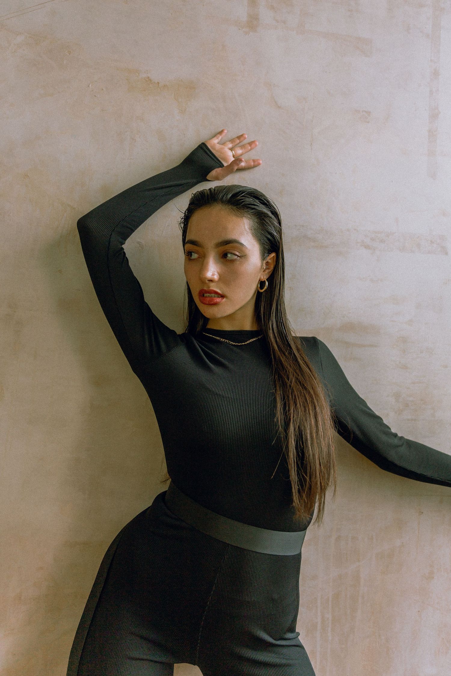 Fashion pose against beige wall in fitted black athletic wear.