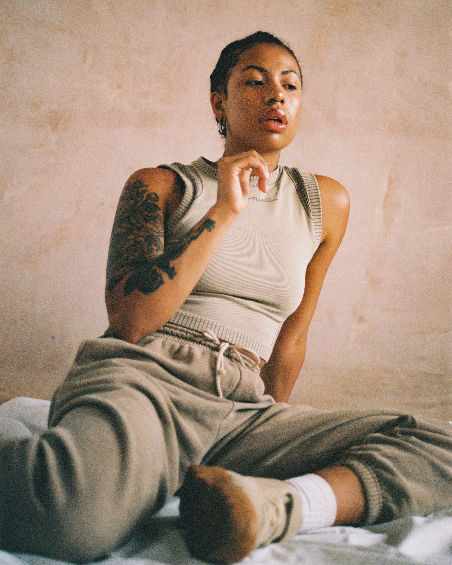 Athletic style portrait in neutral tones with distinctive arm tattoo artwork.