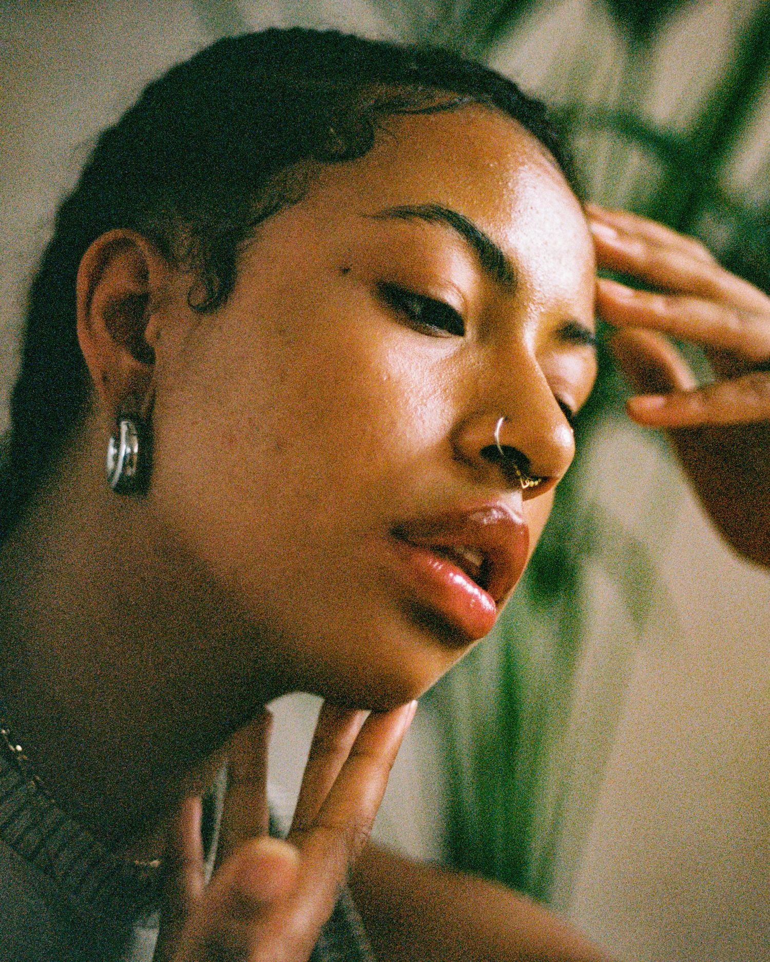 Artistic portrait featuring a nose piercing and delicate hand gestures against a blurred background.
