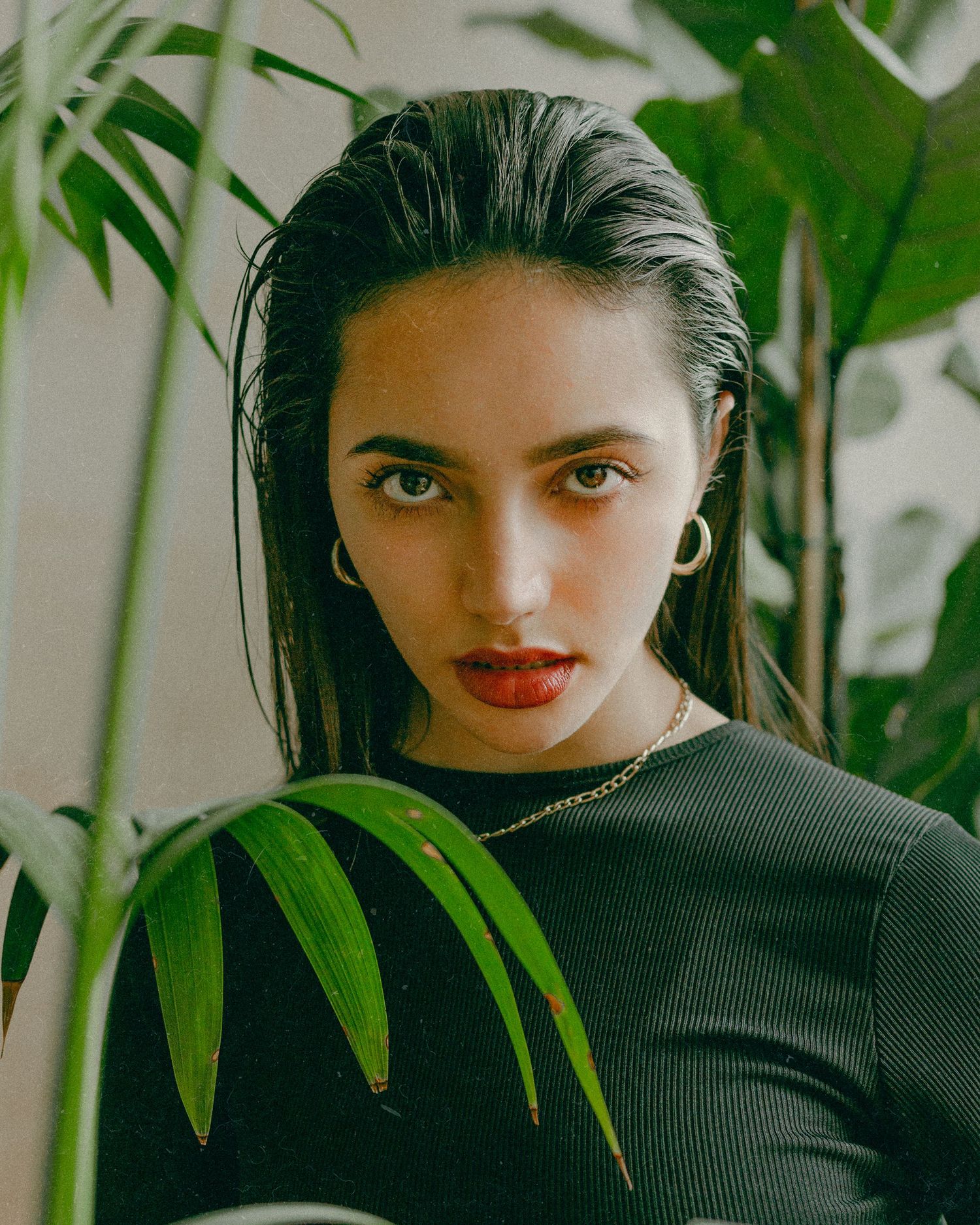 Stylish portrait with monstera leaves in background showcasing elegant makeup and jewelry.