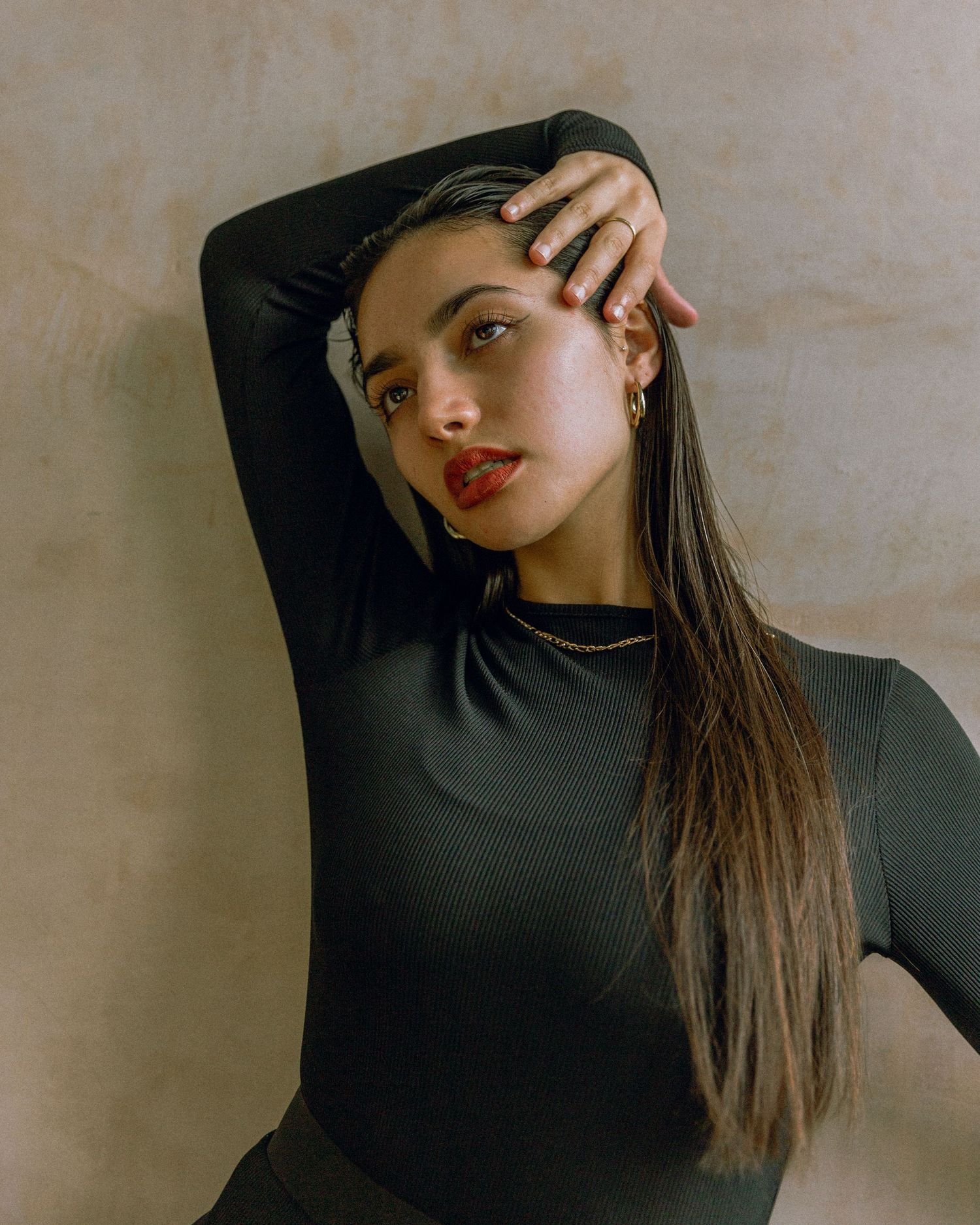Studio portrait against beige wall featuring sleek hairstyle and black top.