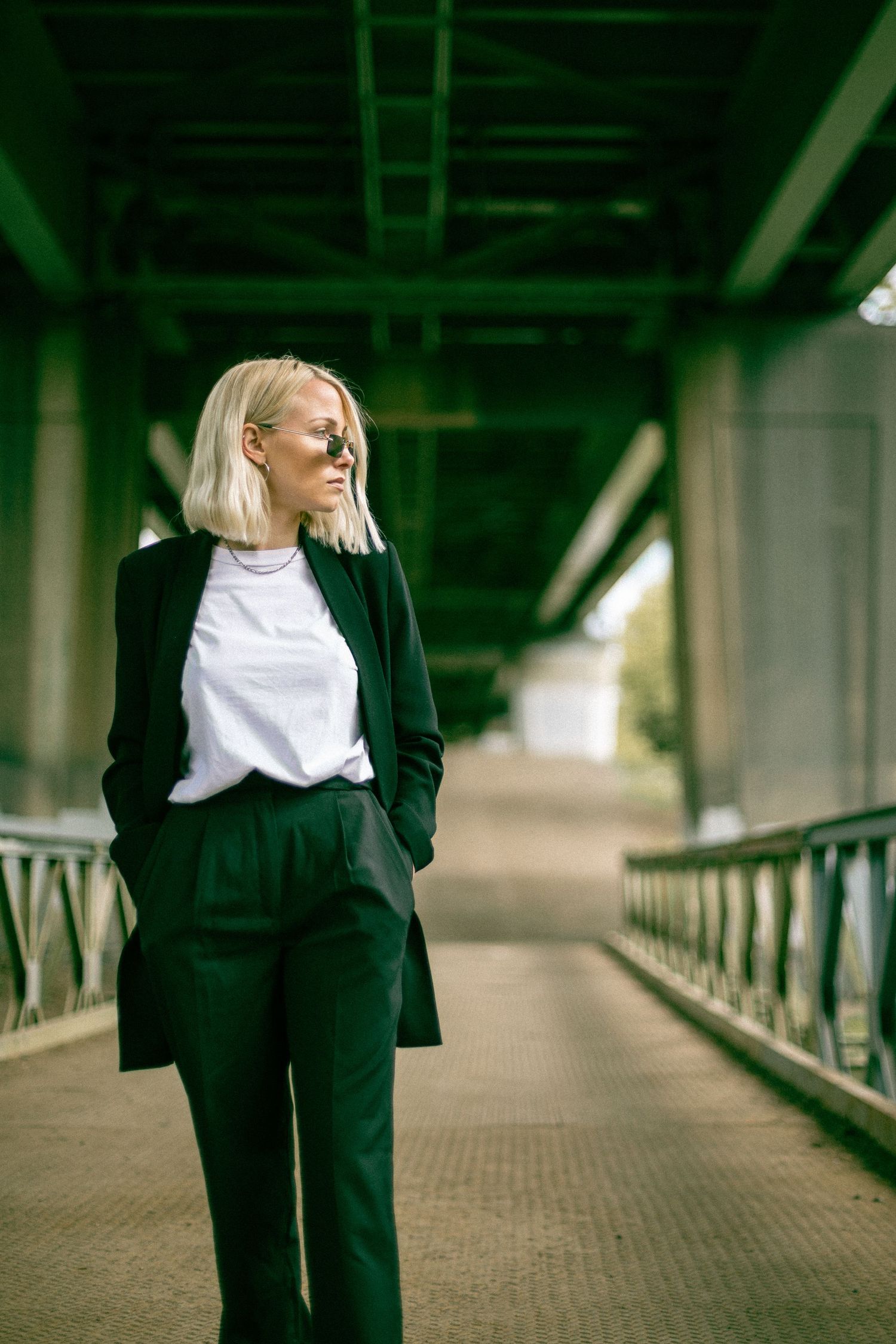 Fashion photo series showing artistic poses along an industrial bridge walkway wearing black and white outfit.