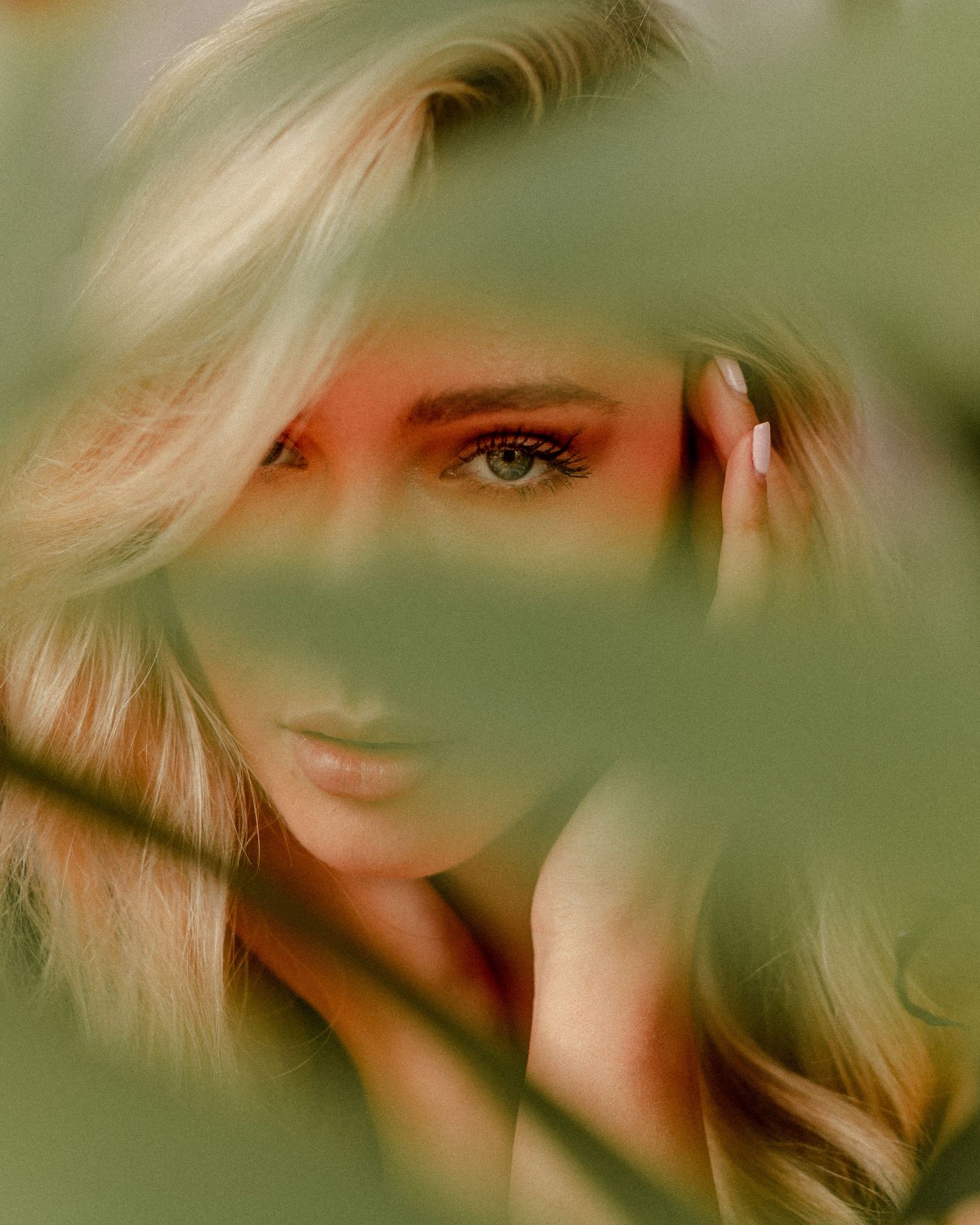 Dreamy portrait through green leaves creating soft bokeh effect.