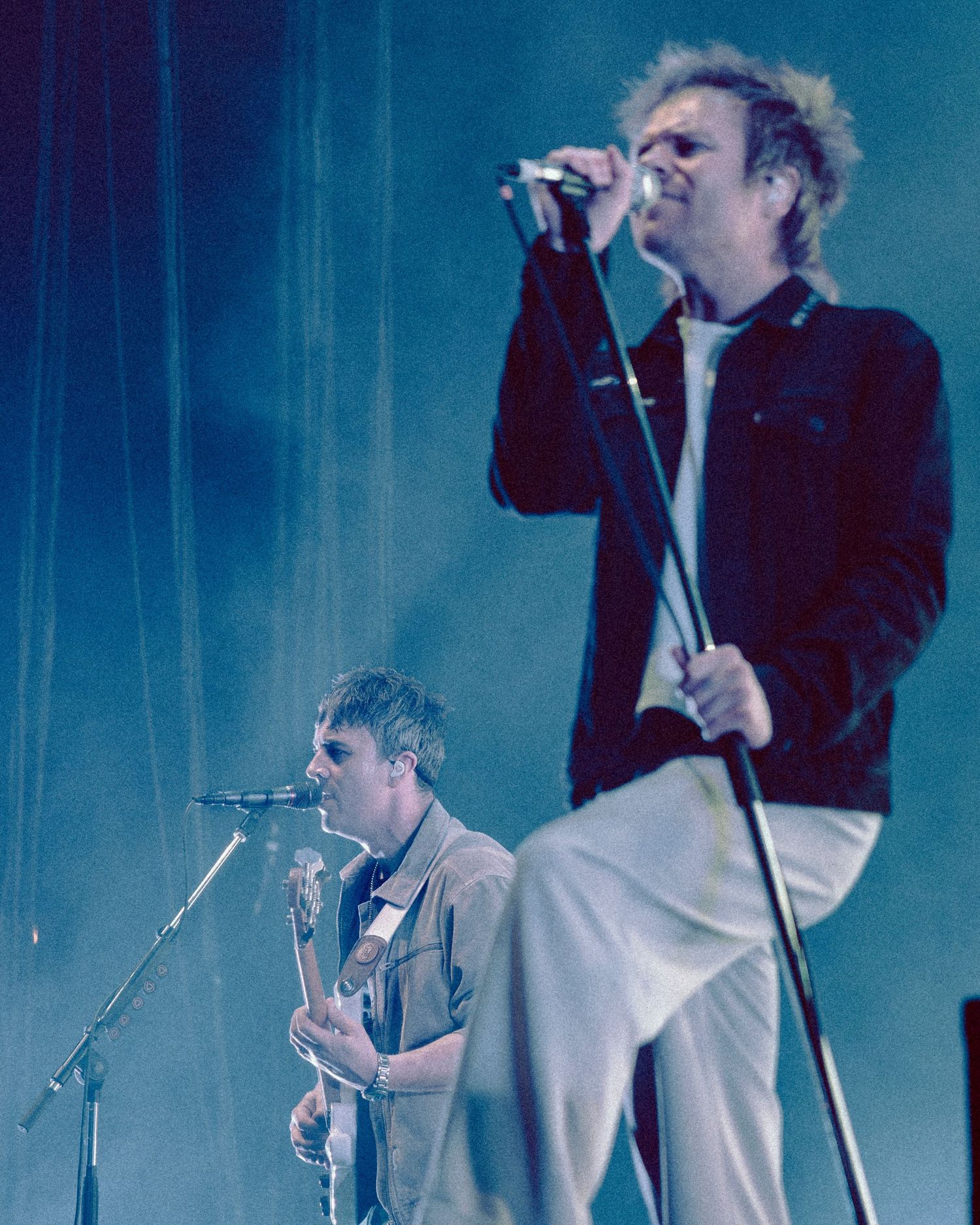 Musicians perform on stage with dramatic blue lighting and fog effects during a concert performance.