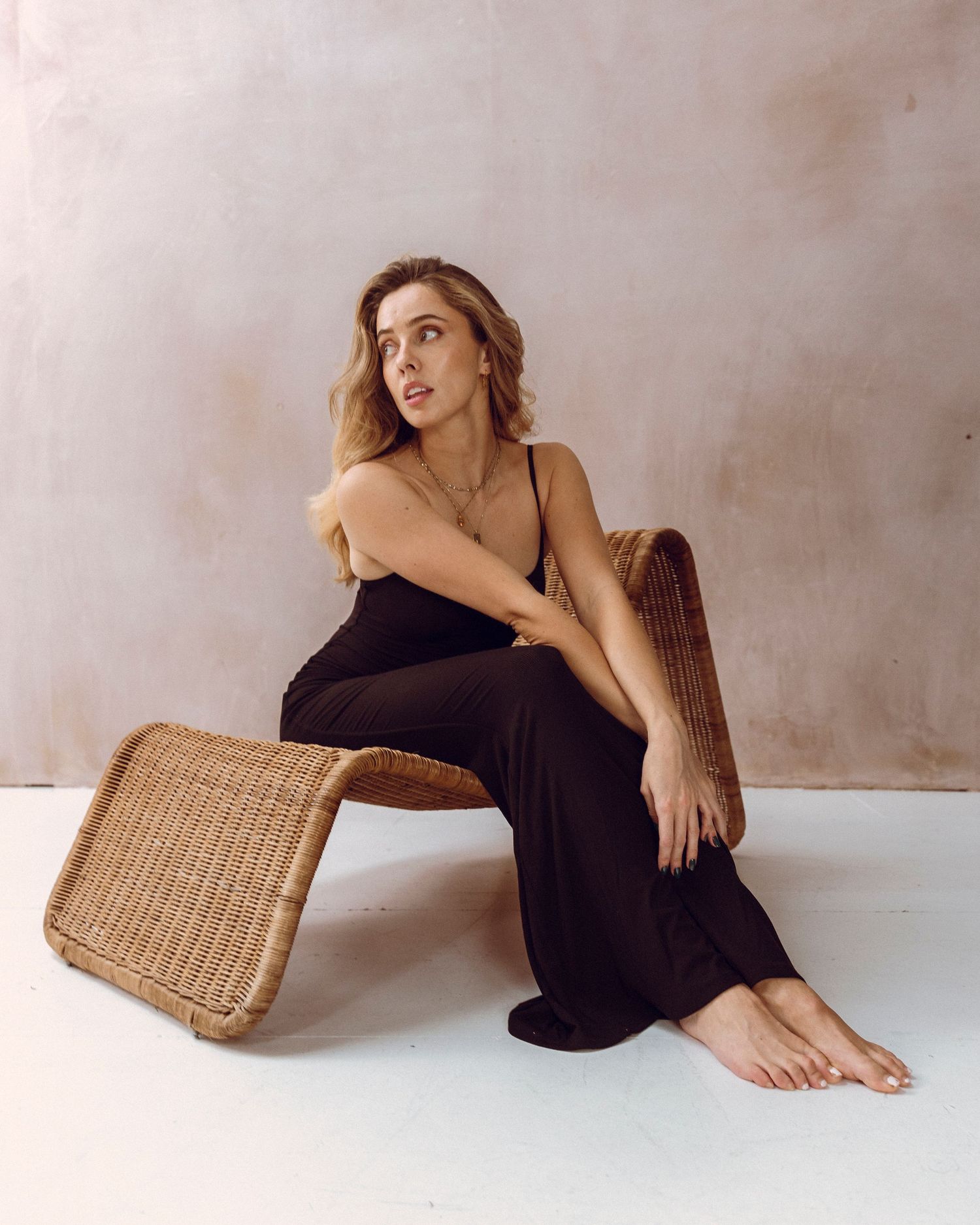 Minimalist fashion portrait with wicker furniture against neutral beige wall.