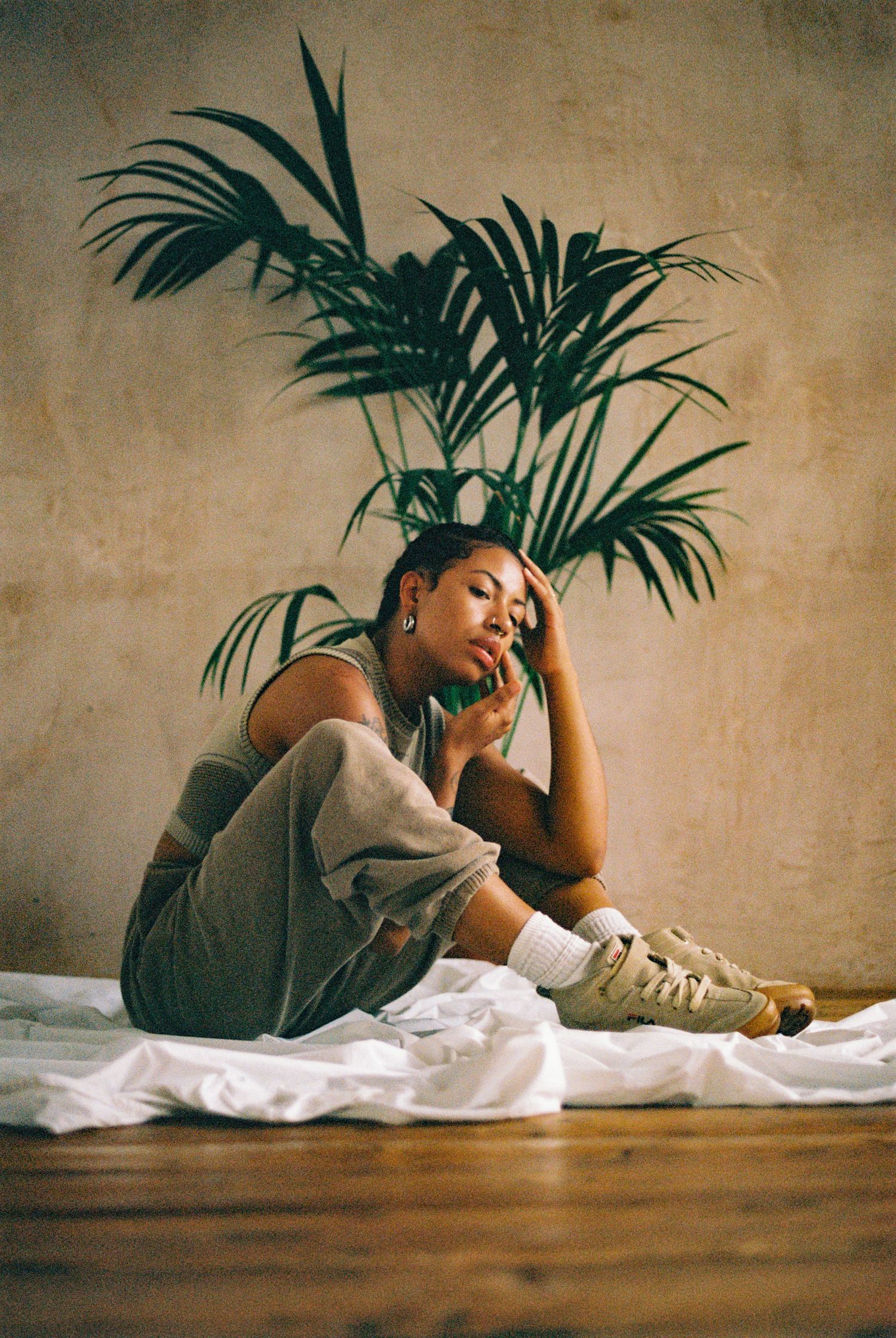 Relaxed pose against beige wall with palm plant shadow creating artistic composition.