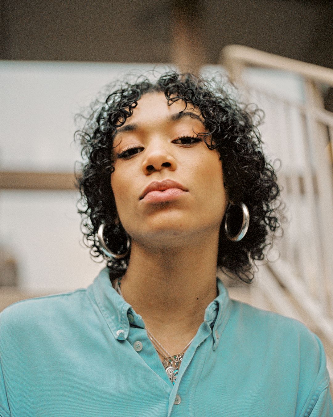 Close-up portrait showing silver hoops and layered necklaces with mint collar shirt.