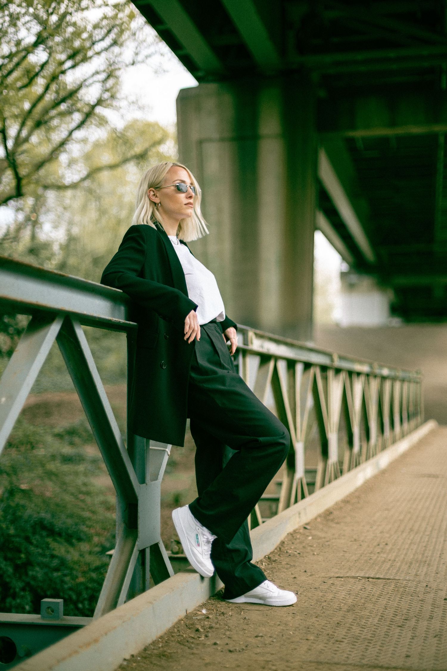 Modern fashion photography showcasing dark clothing against industrial bridge architecture and natural scenery.