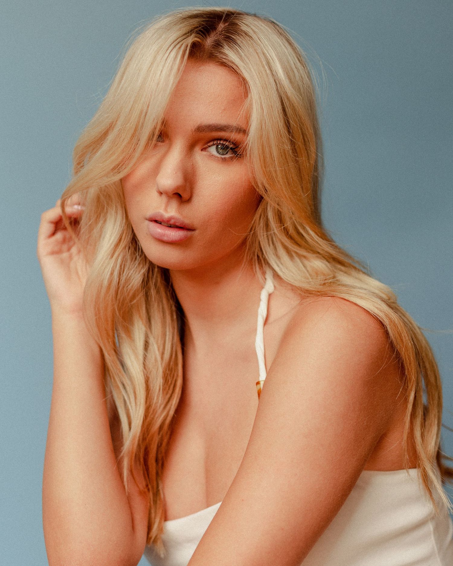 Close-up beauty shot showcasing blonde waves and natural makeup against blue backdrop.