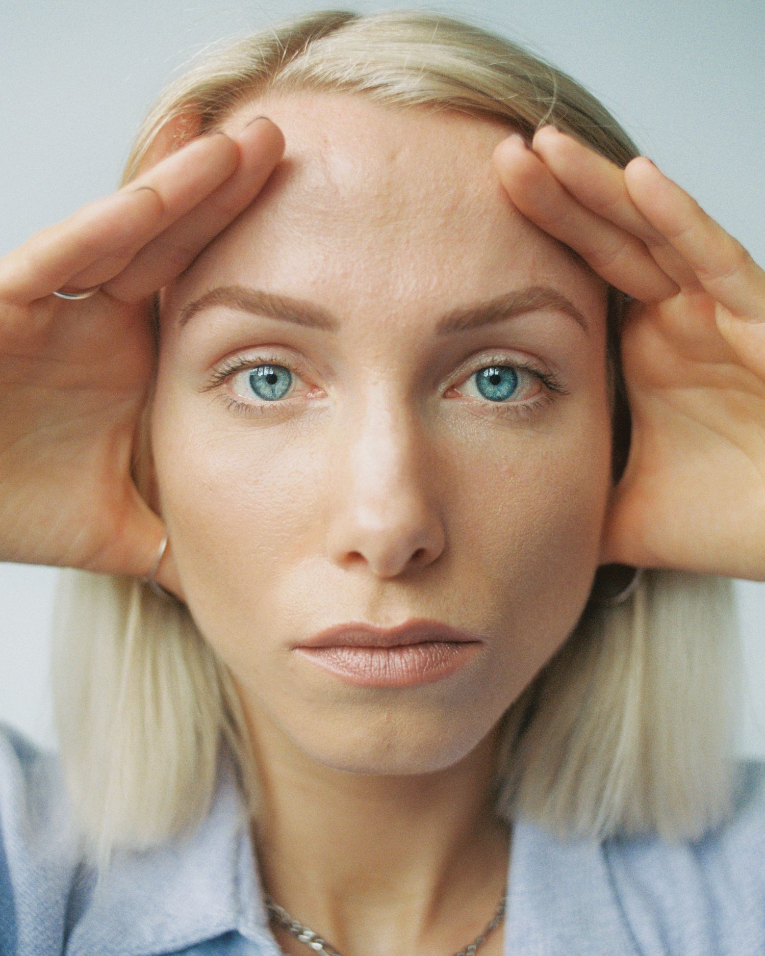 Close-up beauty portrait with hands framing face and striking blue eyes.