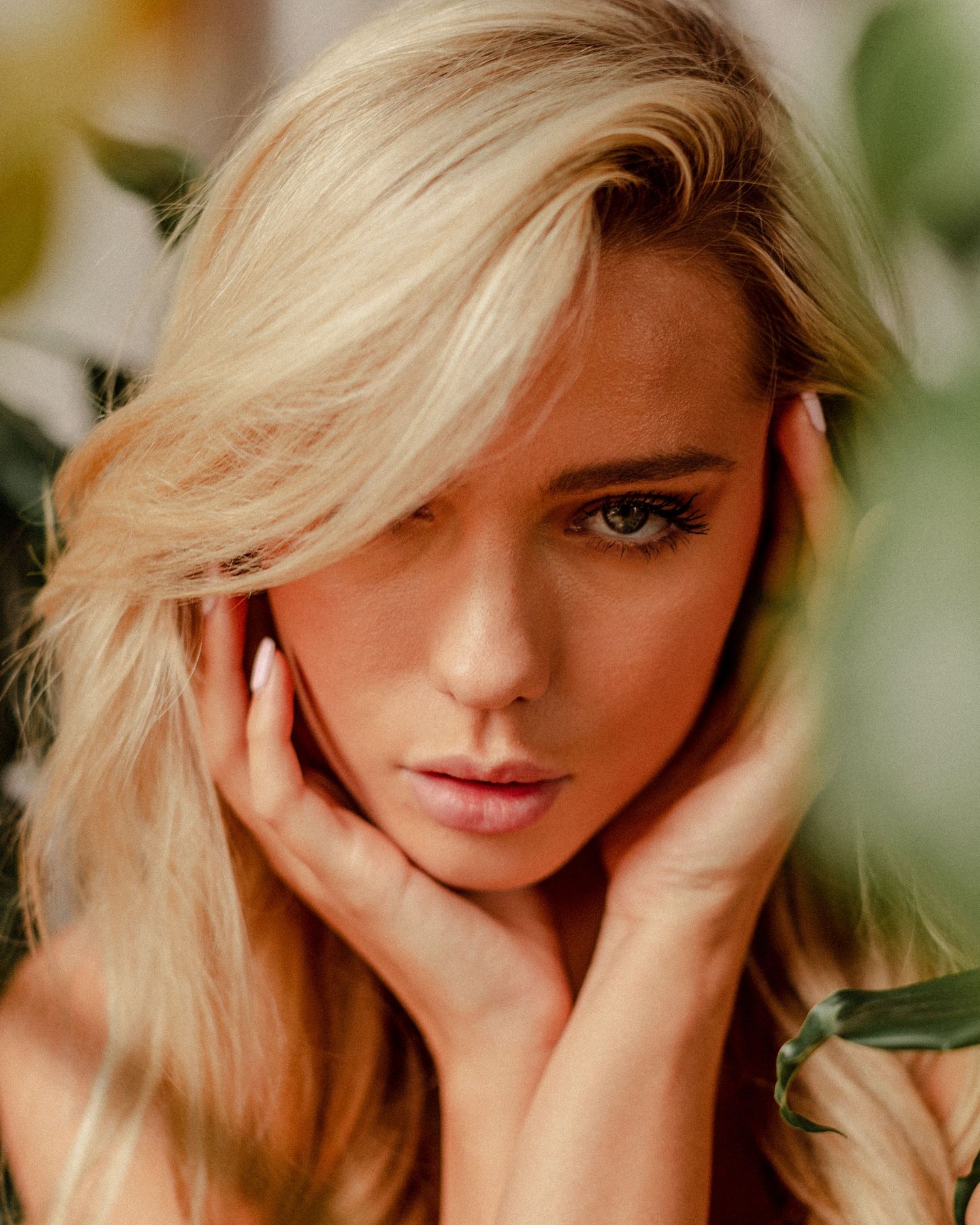 Glamour portrait featuring blonde hair and subtle makeup with hands framing face.