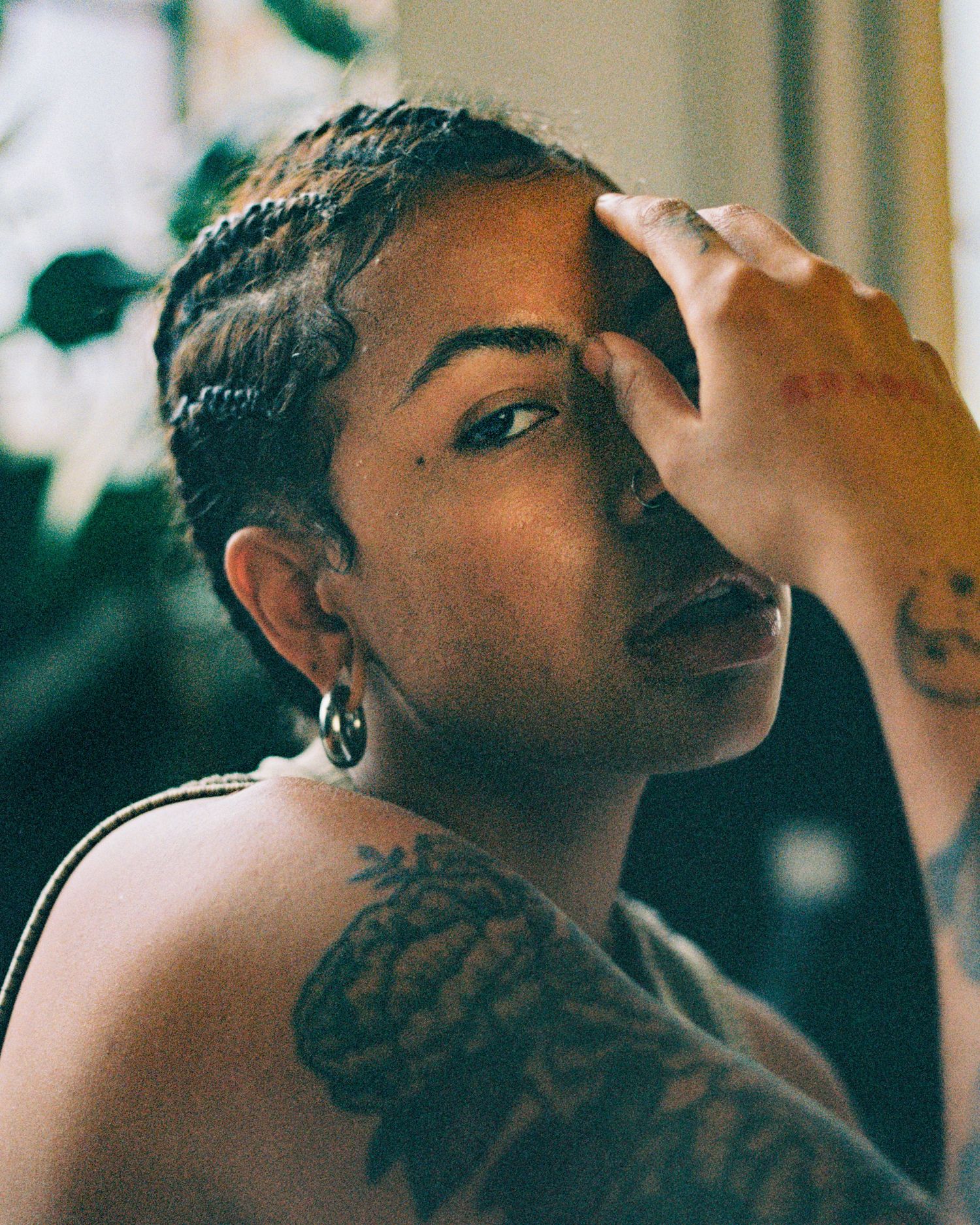 Artistic portrait highlighting tattoo and ear gauges in soft lighting.
