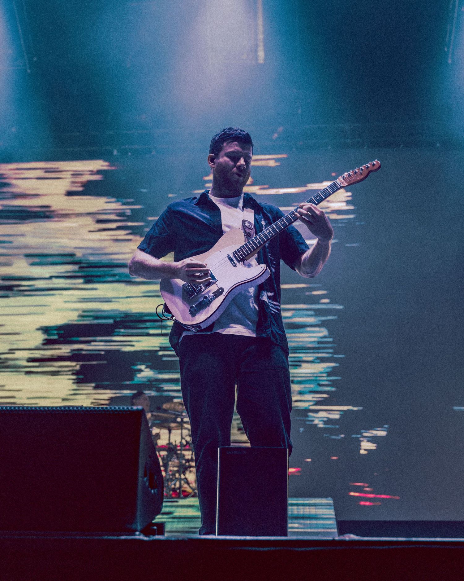 Musician on stage playing an electric bass guitar against a dark background with blue lighting effects.
