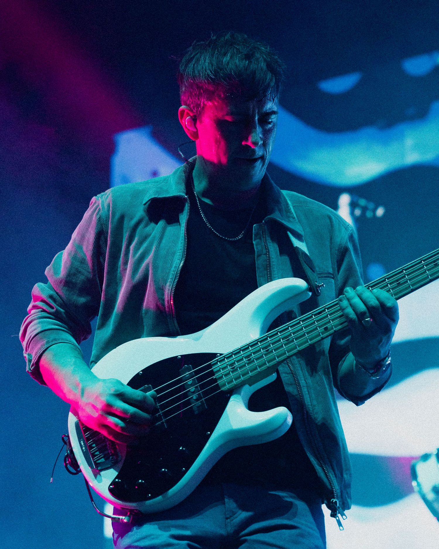 A bassist performs on stage under moody blue and pink lighting creating an atmospheric concert ambiance.