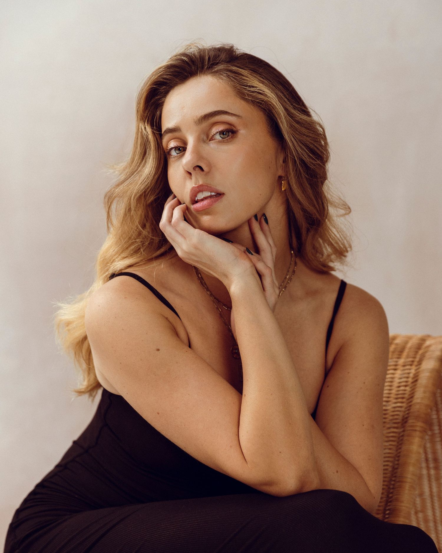 Soft portrait with neutral backdrop featuring black top and natural styling.