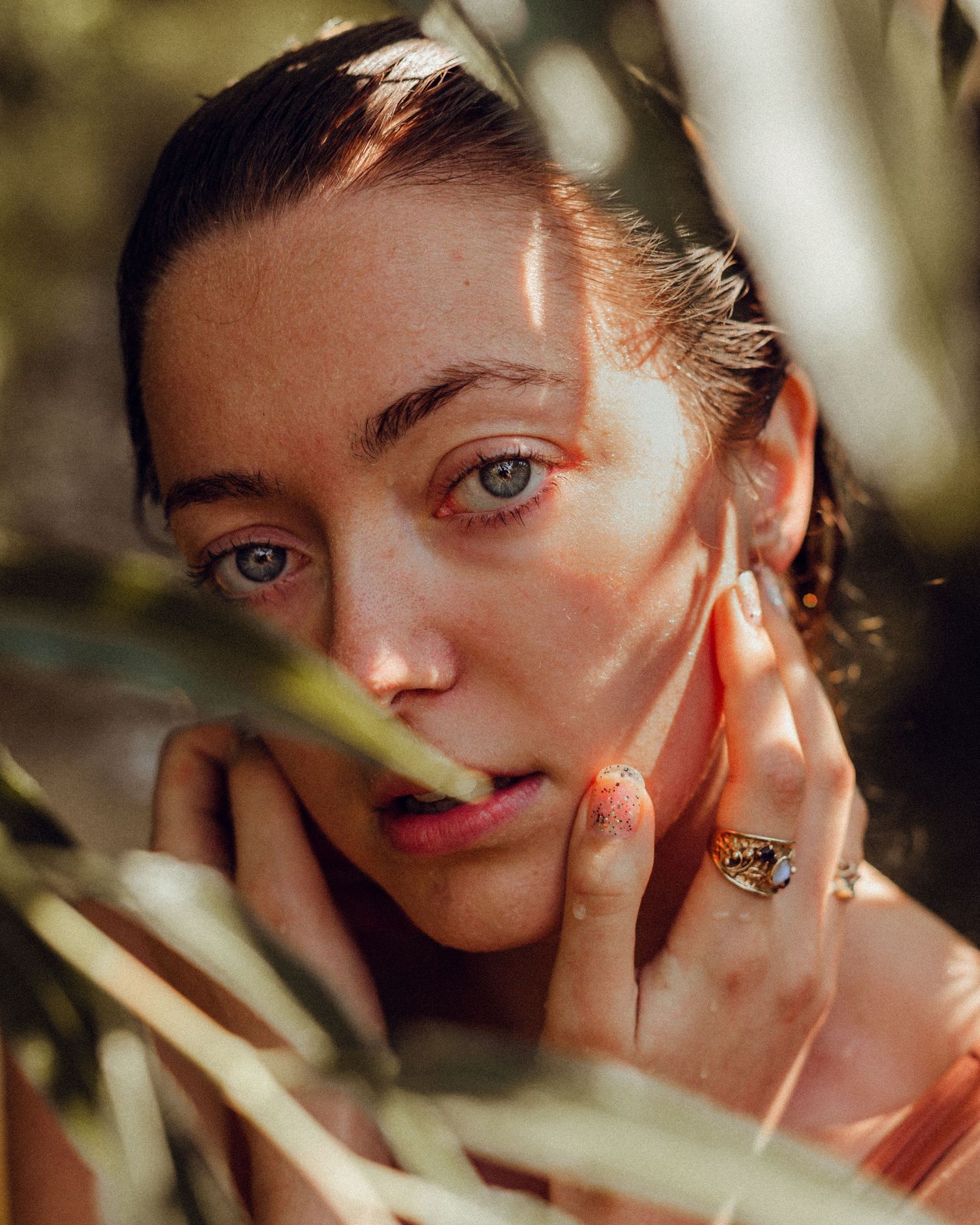Artistic portrait through leaves with natural sunlight creating dappled shadows.