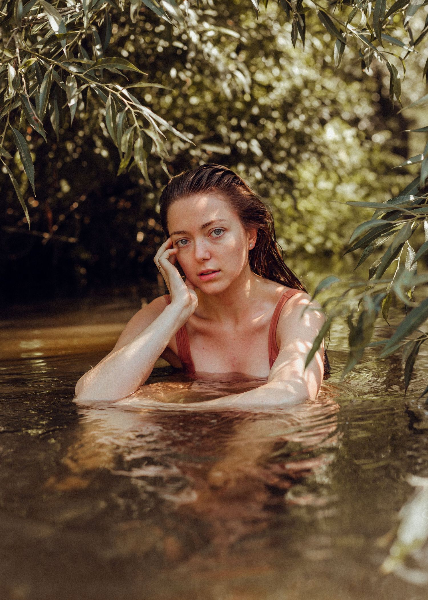 Romantic outdoor portrait in water surrounded by overhanging willow branches.