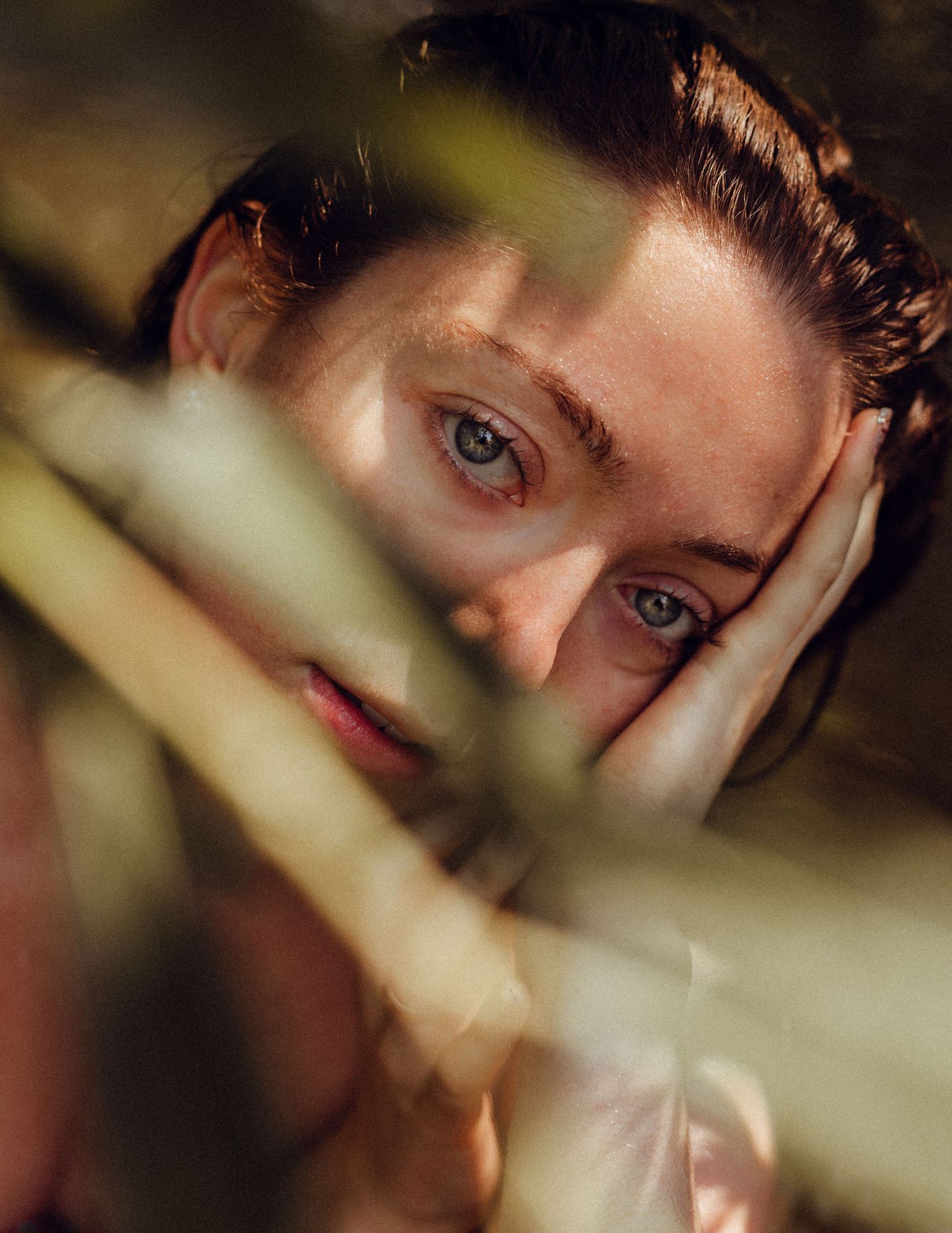 Moody portrait partially obscured by foliage with dramatic shadows and lighting.