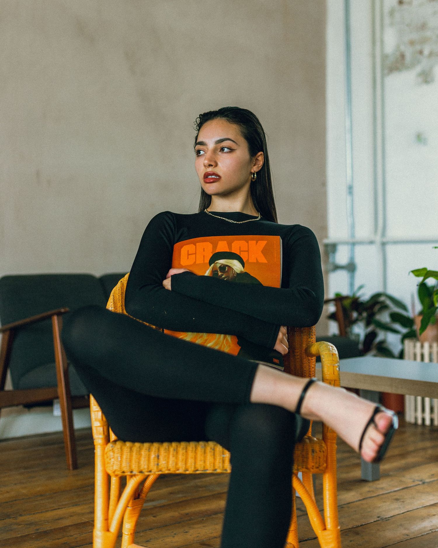 Fashion model in black outfit poses on vintage yellow rattan chair.