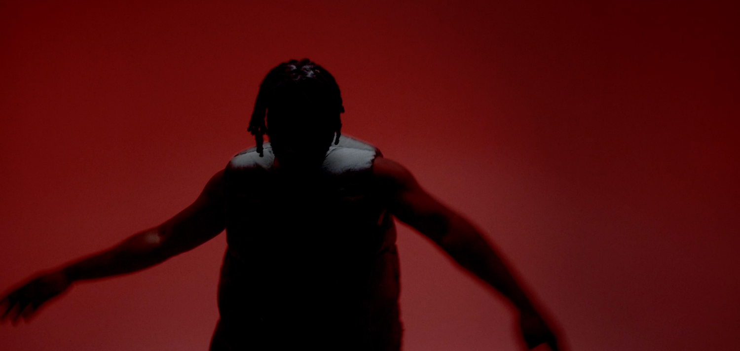 Dark silhouette posing dramatically against deep red backdrop.
