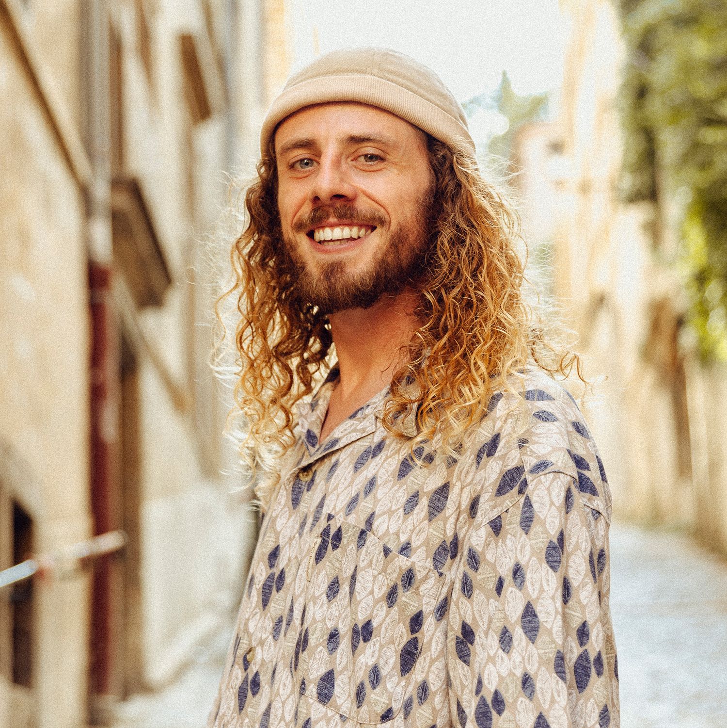 Portrait series of person in patterned shirt with long curly hair against urban backdrop.