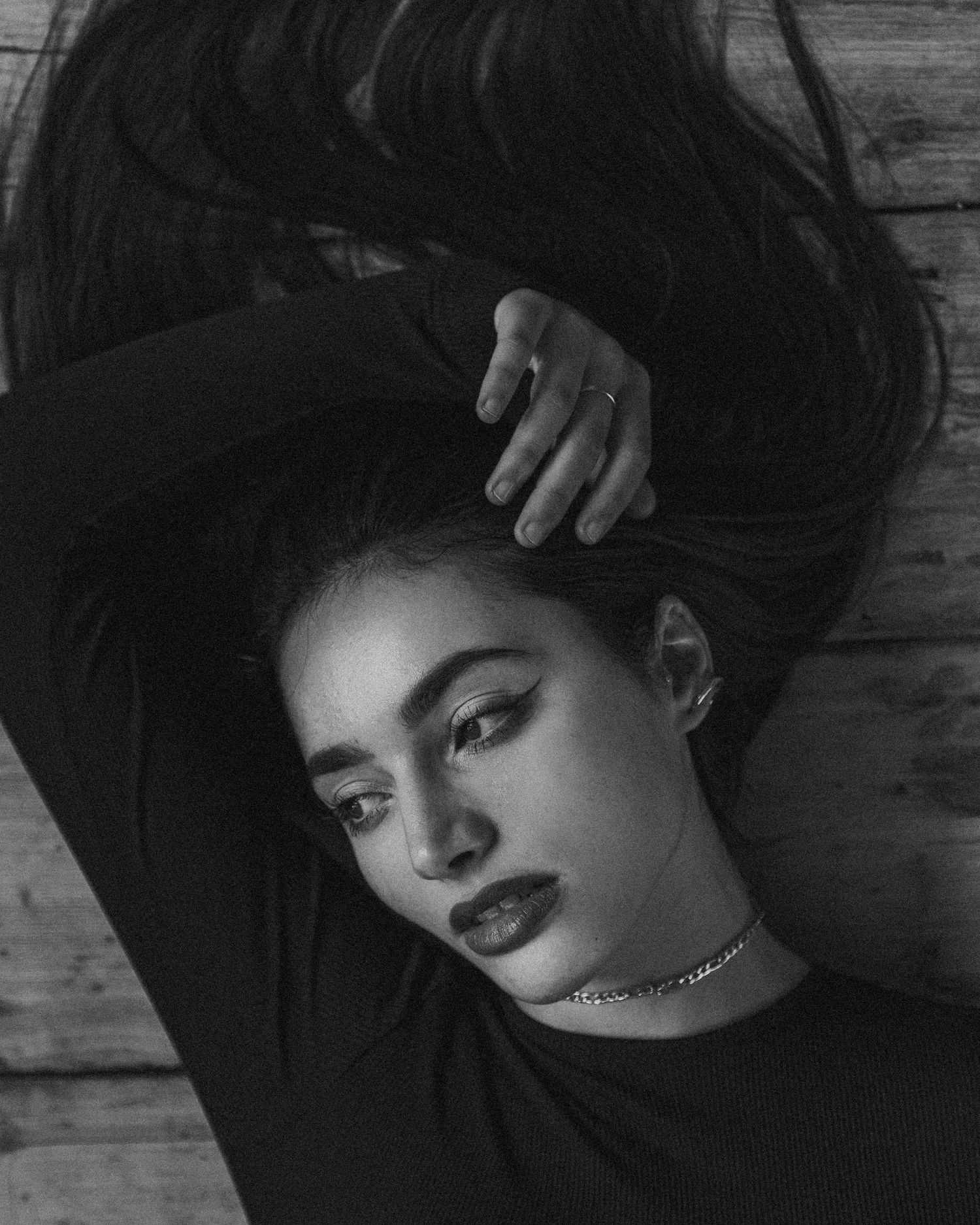 Moody portrait with extended arm pose and choker necklace on wooden surface.